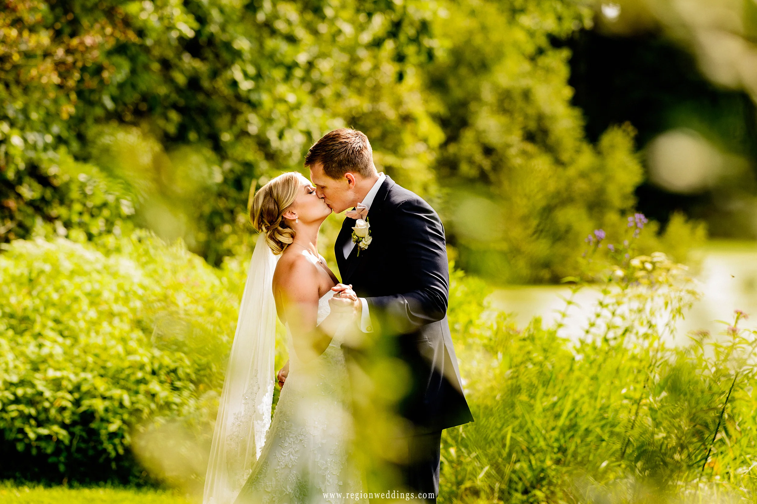 Bride and groom share in a kiss amidst the nature of Taltree Arboretum.