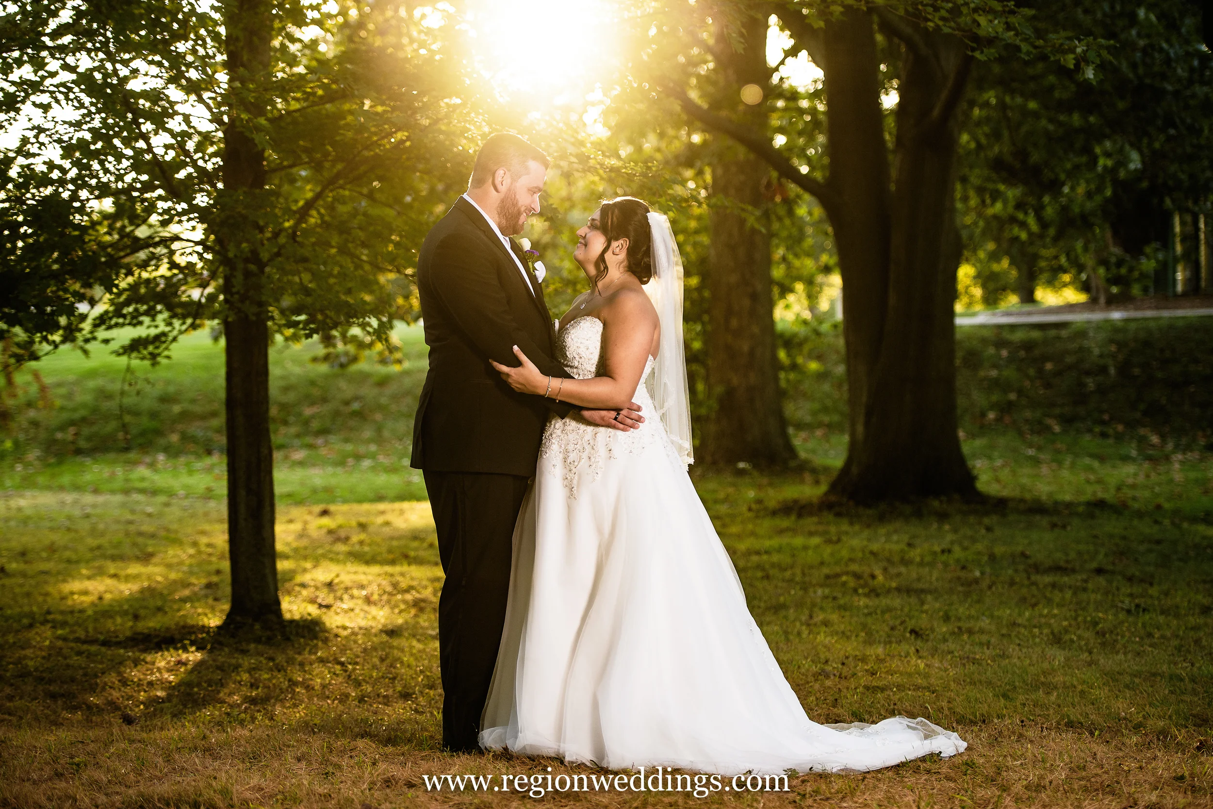 The sun sets as the bride and groom gaze at each other beneath the tall trees in the forest.