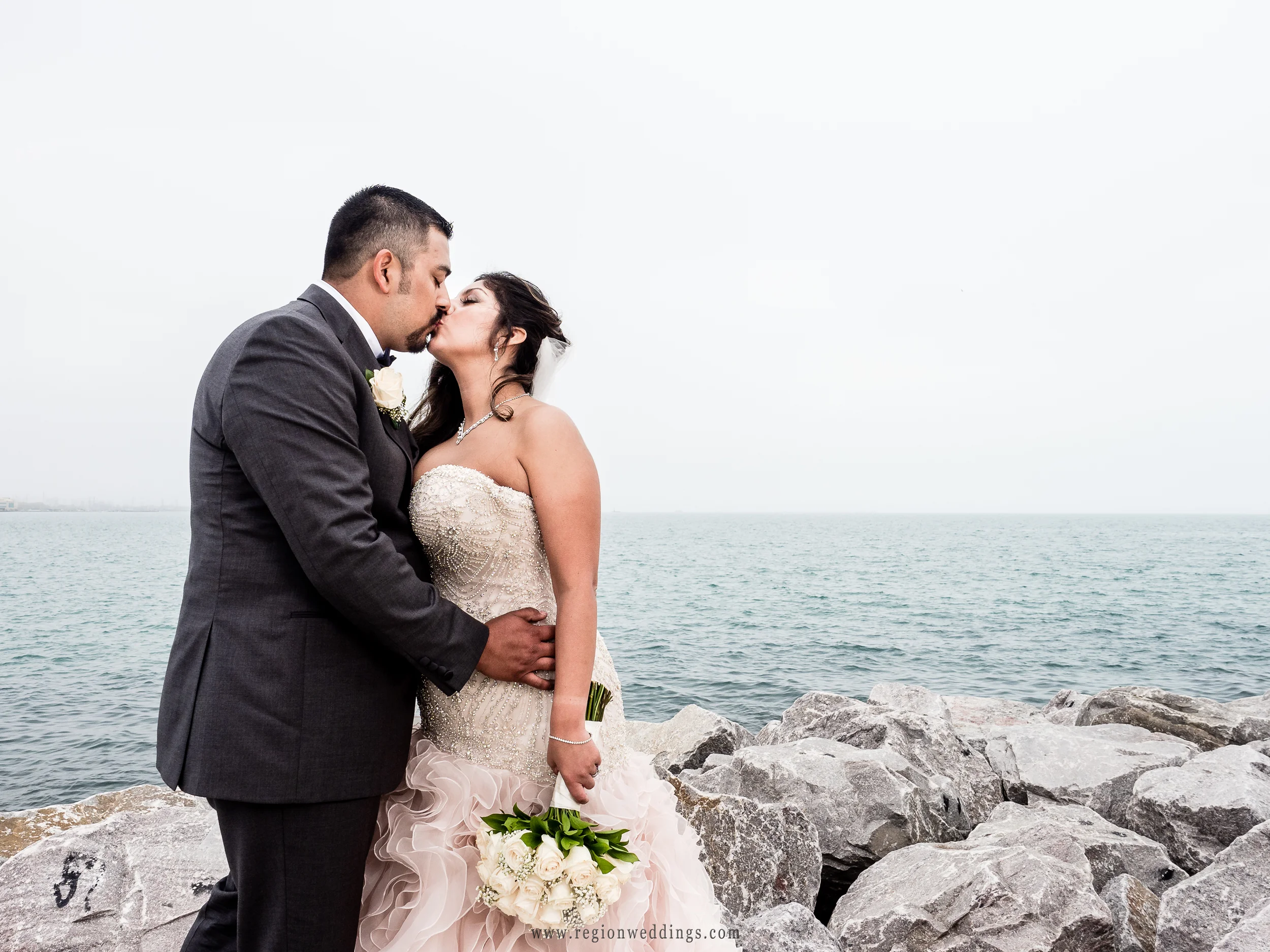 Bride and groom smooch atop the rocks at Whiting Lake Front Park shoreline.