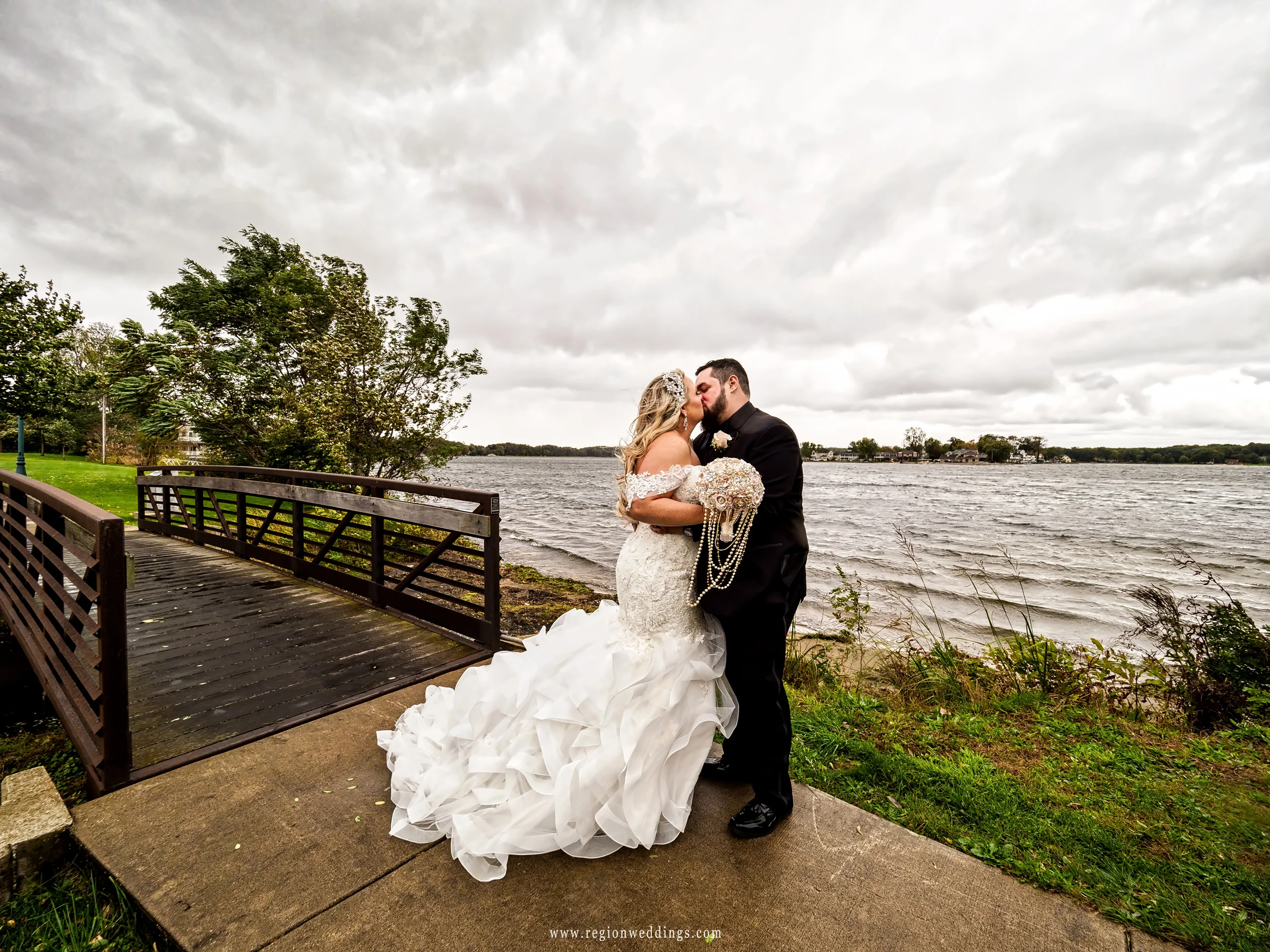 Storm clouds fill the sky as the bride and groom kiss on the edge of Pine Lake in Laporte, Indiana.