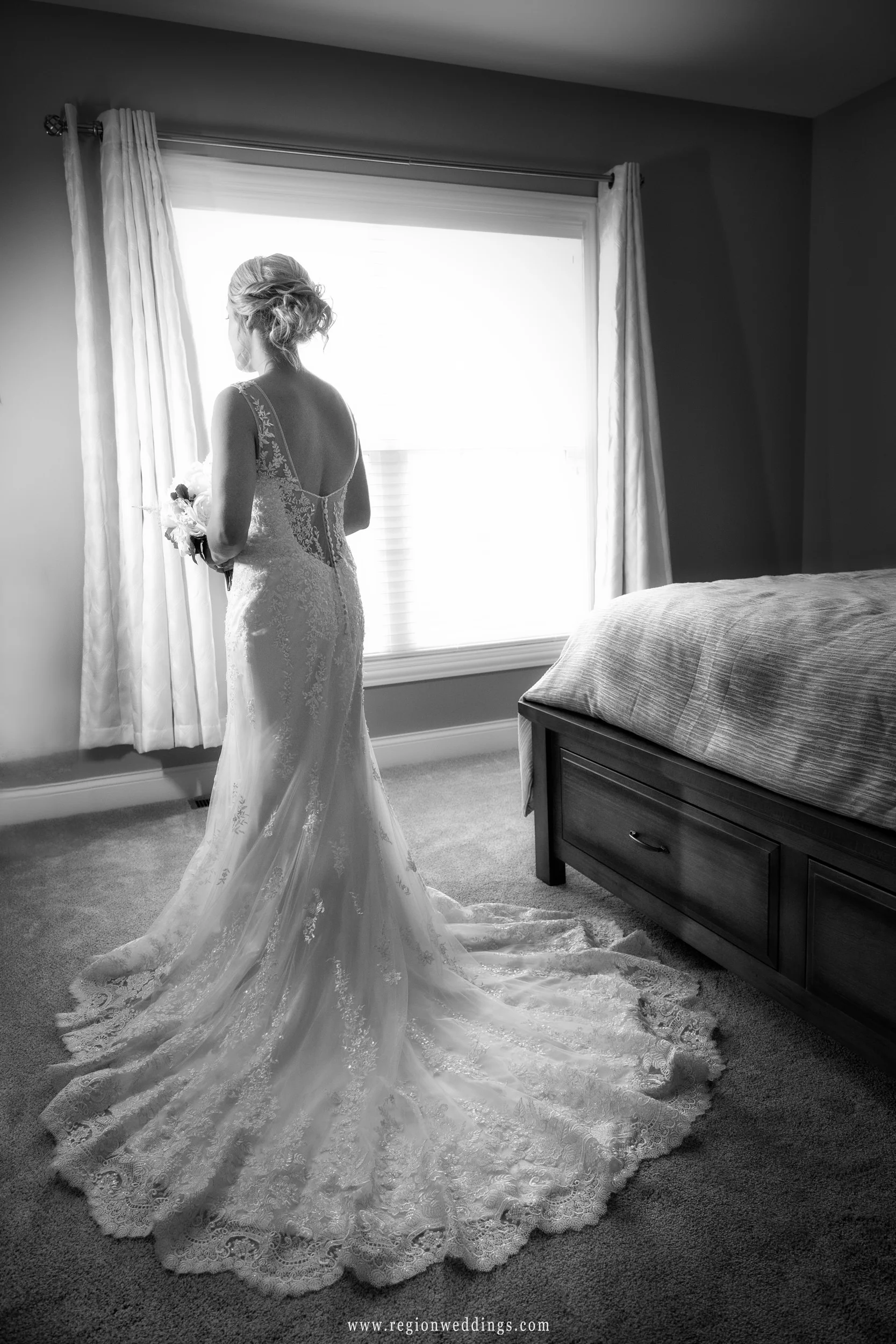 The bride stands alone in her bedroom in her wedding dress.