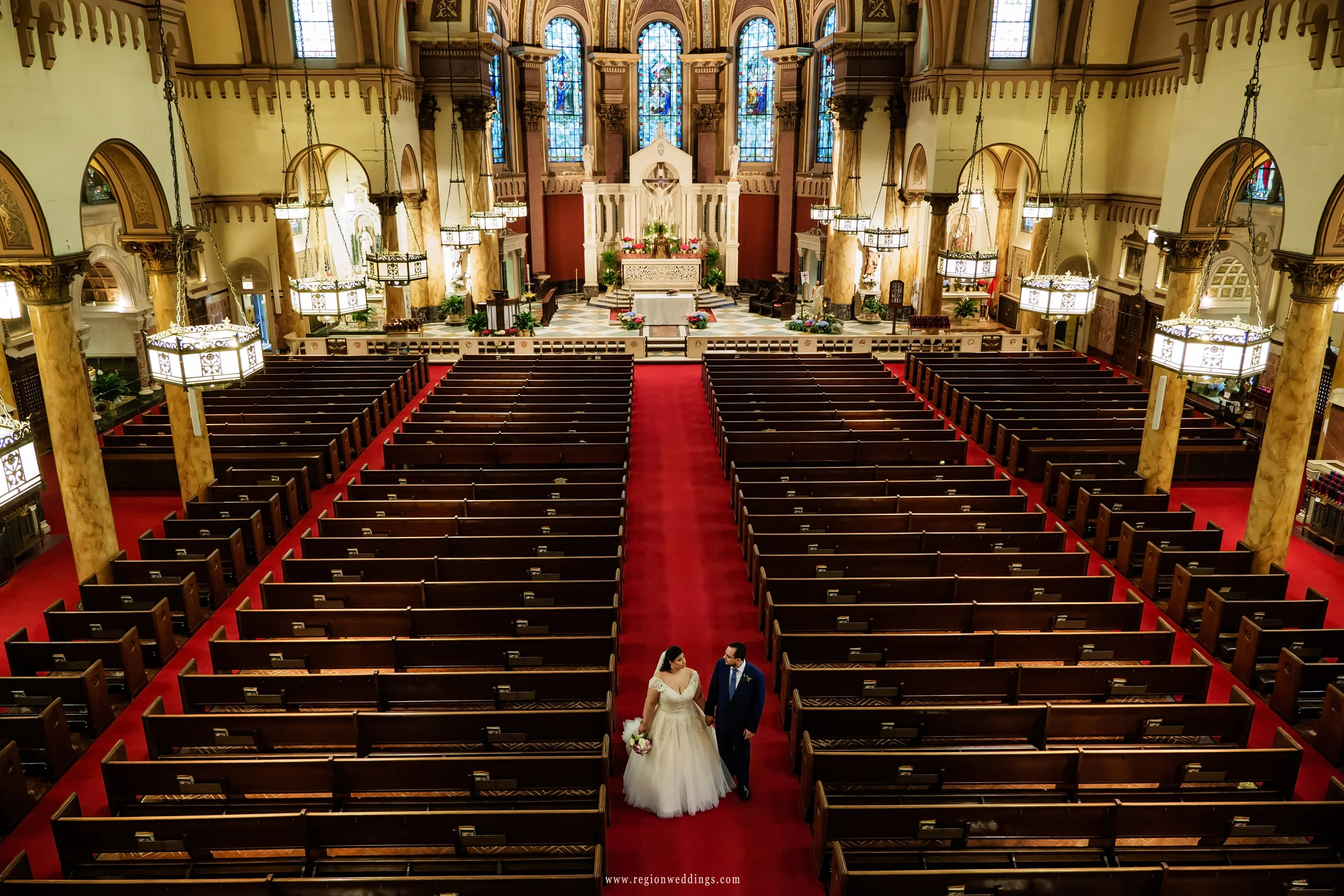 Bride and groom walk toward the church exit of Saint Andrew The Apostle Church.