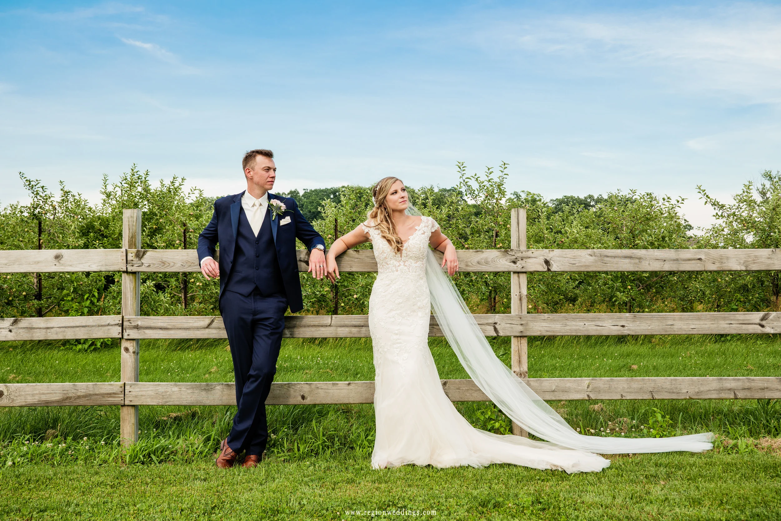 Bride and groom chill against the wooden fence at their rustic wedding venue.