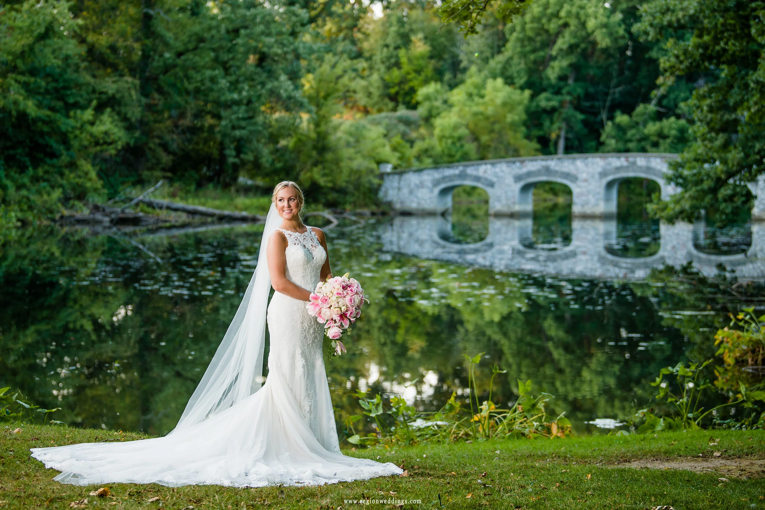 The bride standing near the river as the bridge reflects off the water.