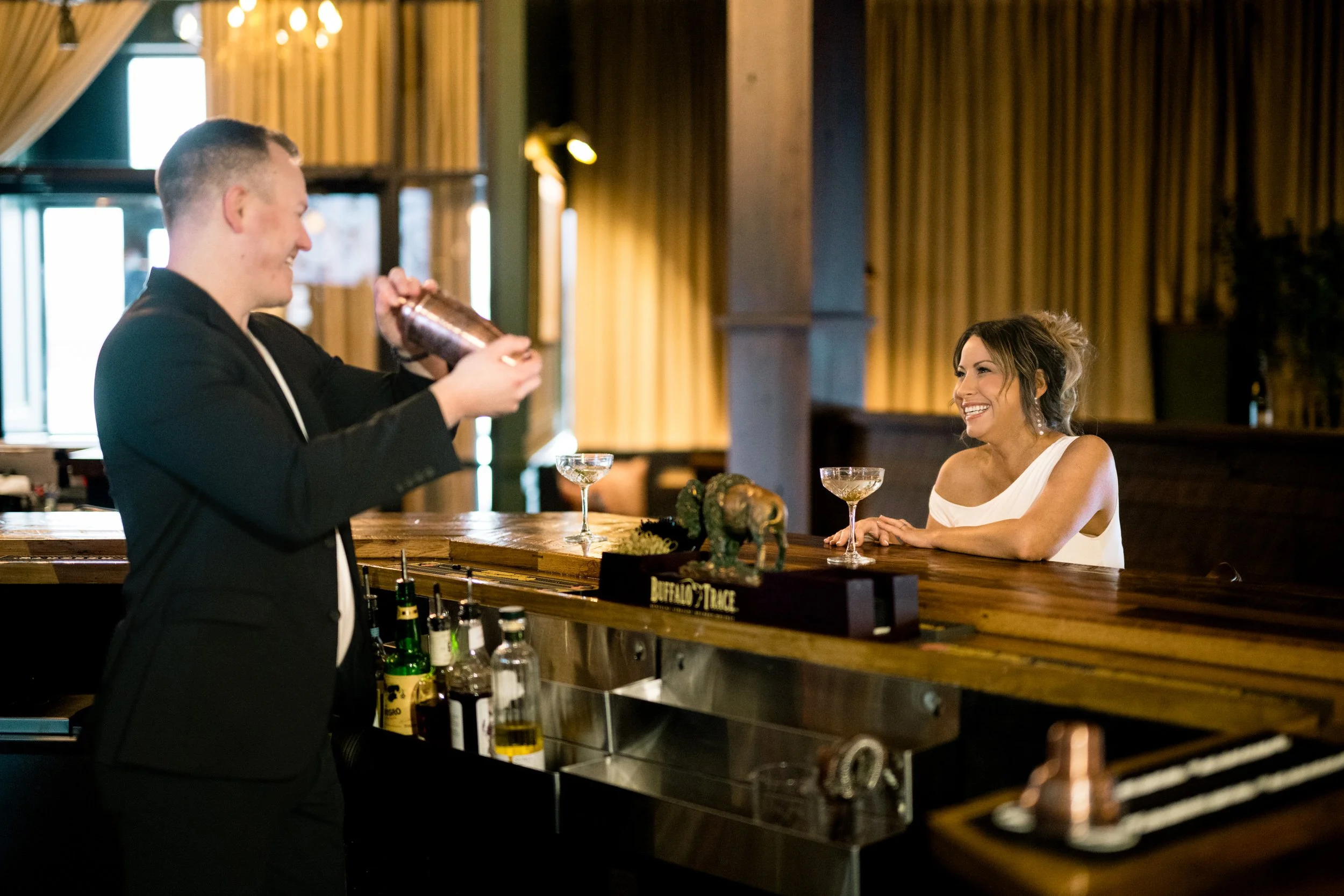The groom steps behind the bar to serve his bride a cocktail.