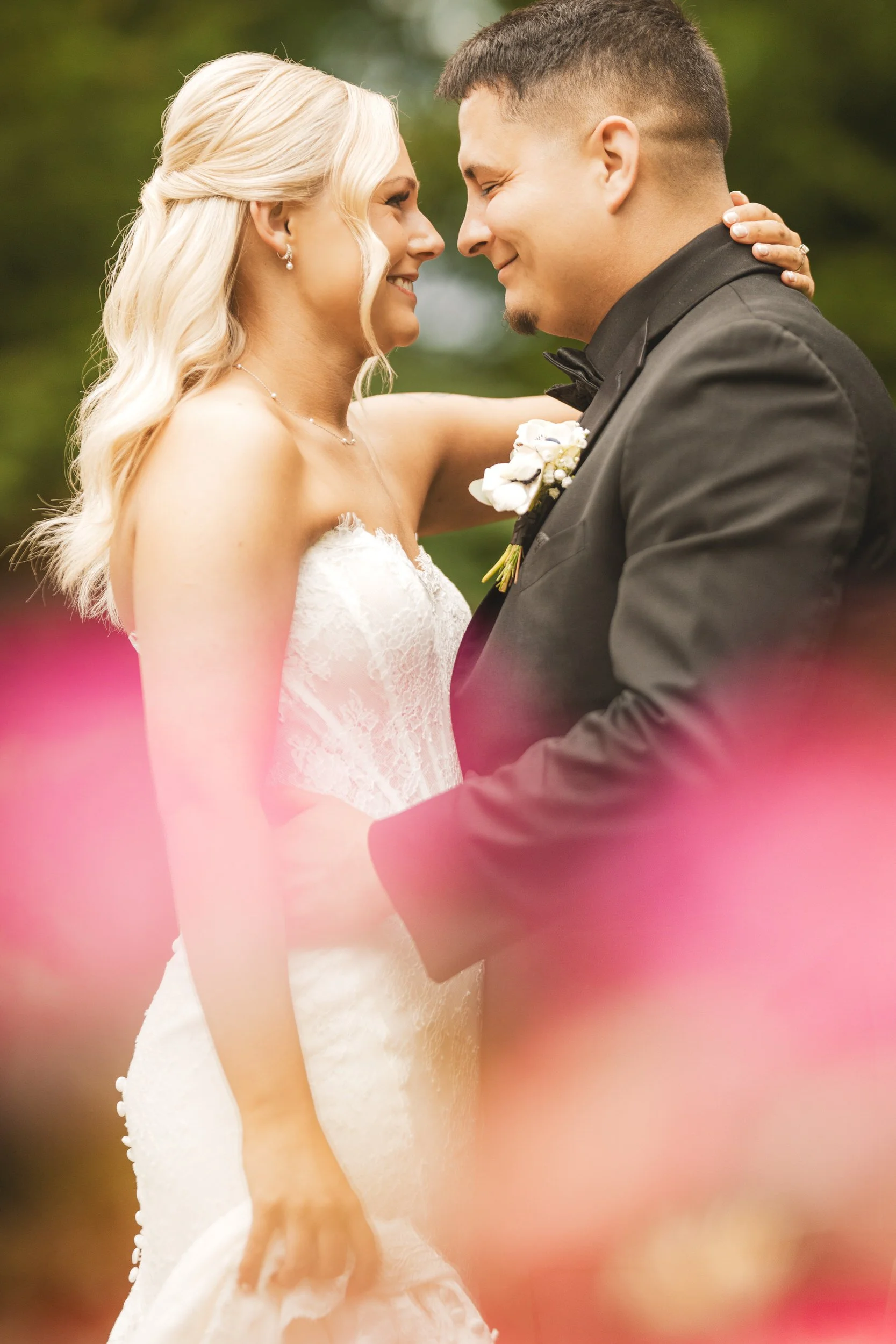 A newly married couple embraces after their wedding ceremony at The Pavilion at Sandy Pines surrounded by pink flowers.