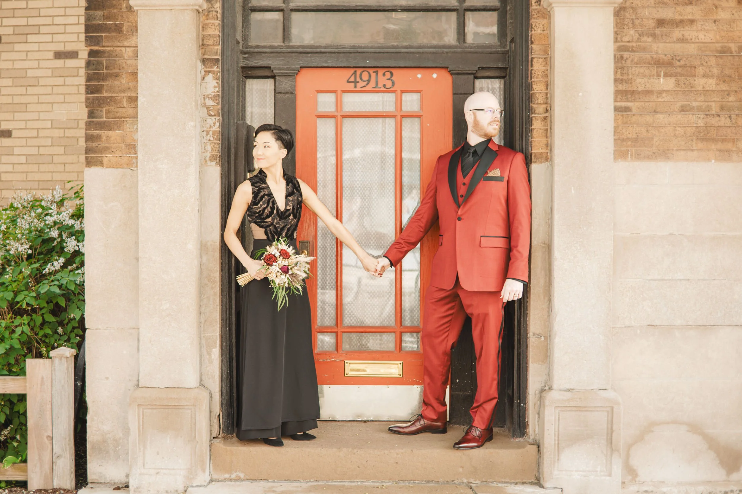 A bride and groom stand in front of a red door on Clark Street in downtown Chicago on their wedding day.