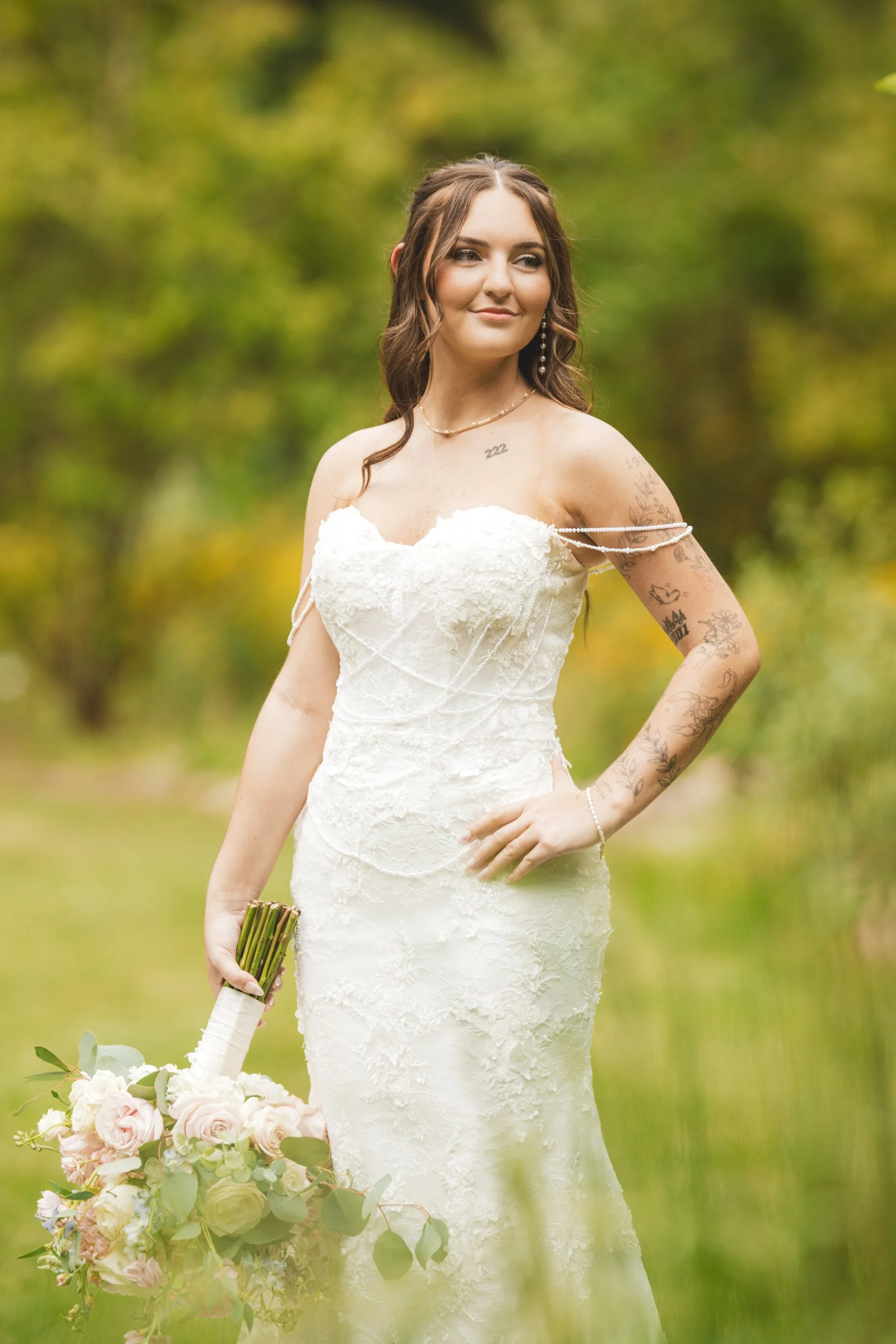 The bride stands in the greenery of Gabis Arboretum in her fitted lace gown wedding dress.