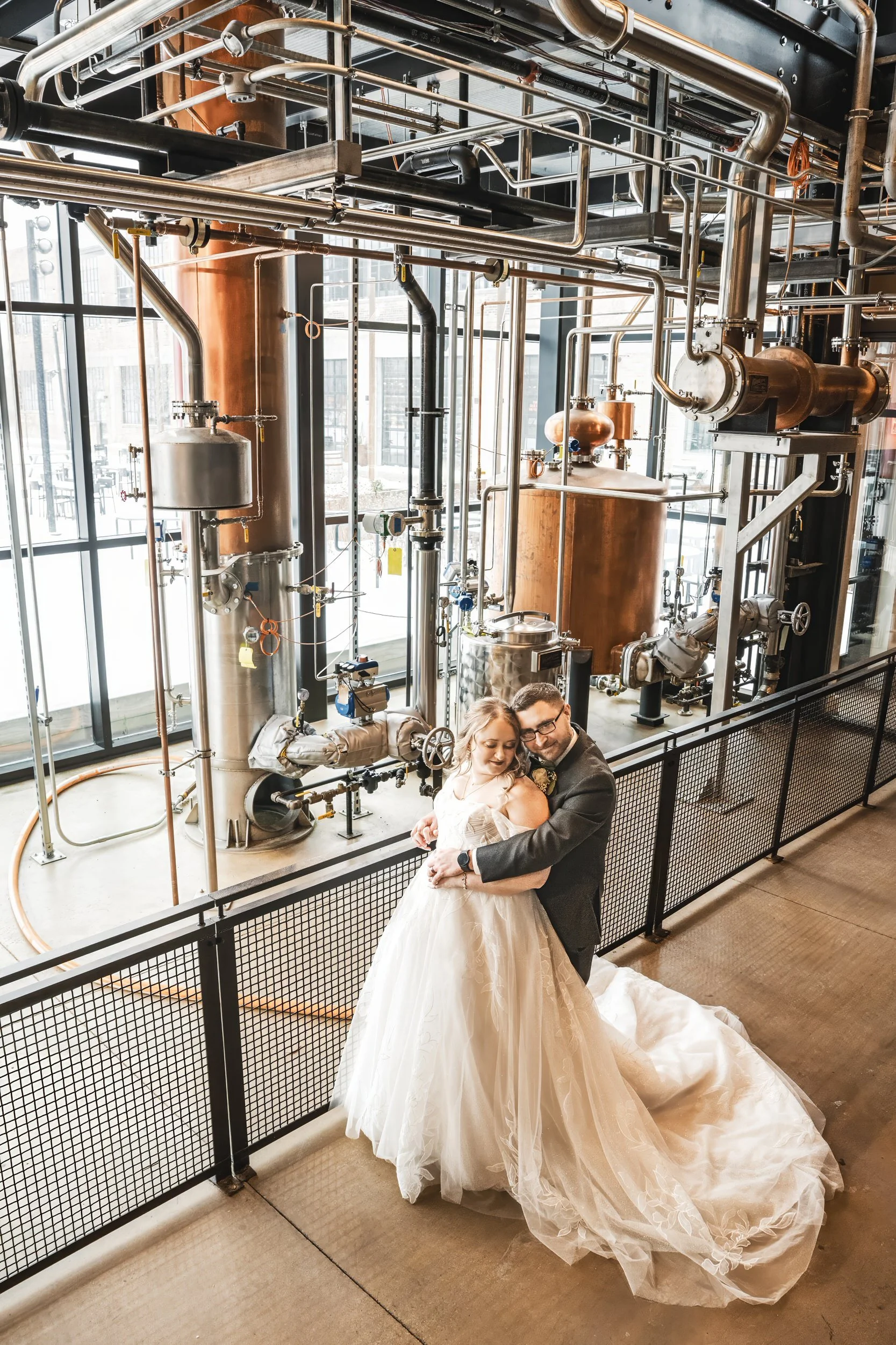 The bride and groom embrace surrounded by the distilling equipment at Journeyman in Valparaiso, Indiana.