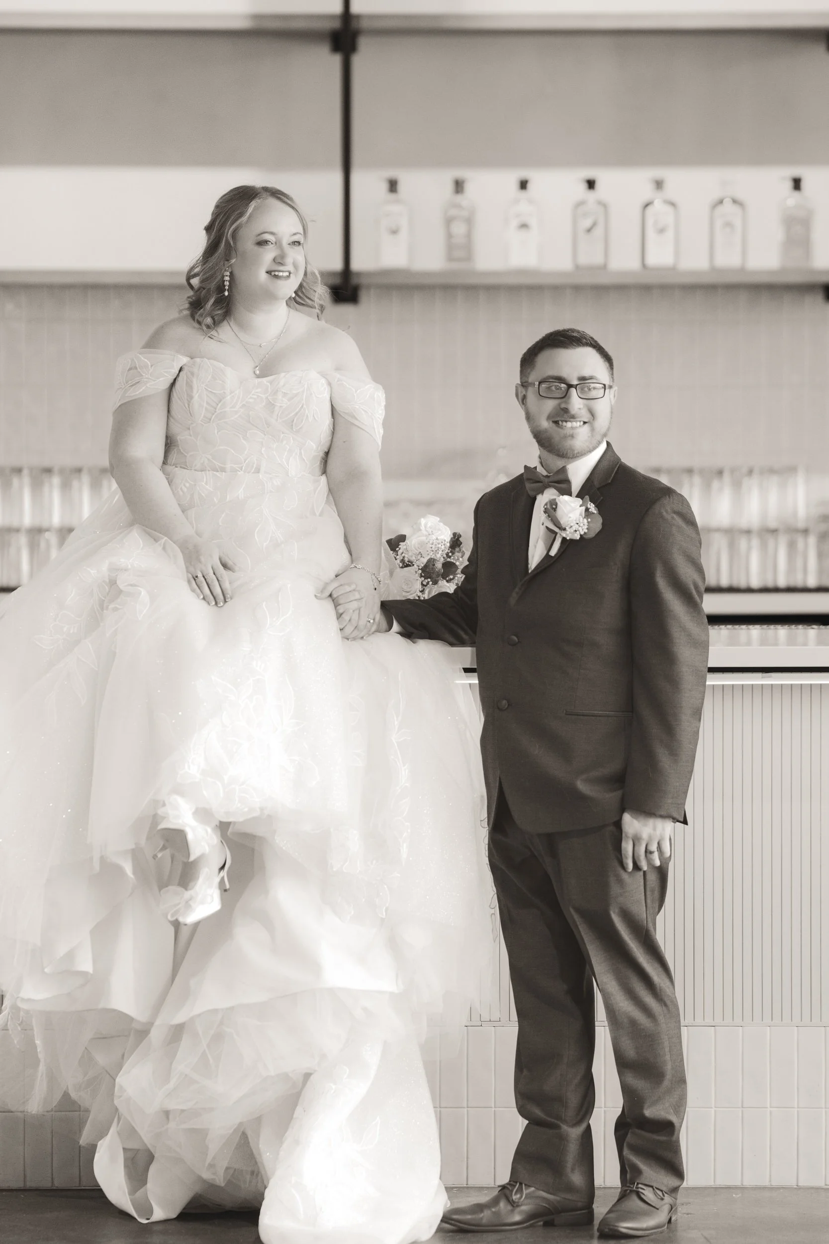 The bride and groom sit on the bar at Journeyman Distillery in Valparaiso, Indiana.