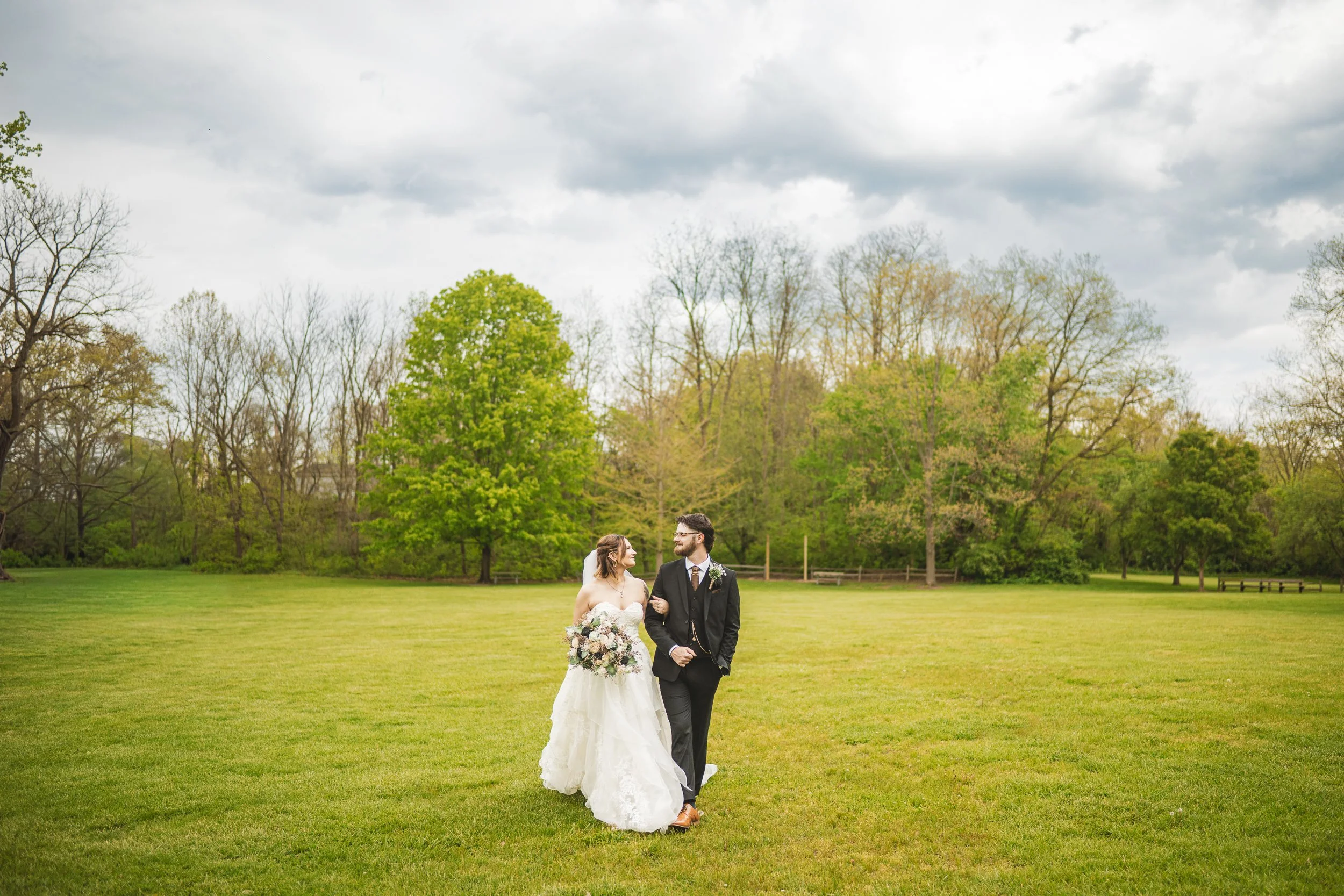 Clouds form in the sky as the bride and groom walk in a greenfield at Deep River County Park.