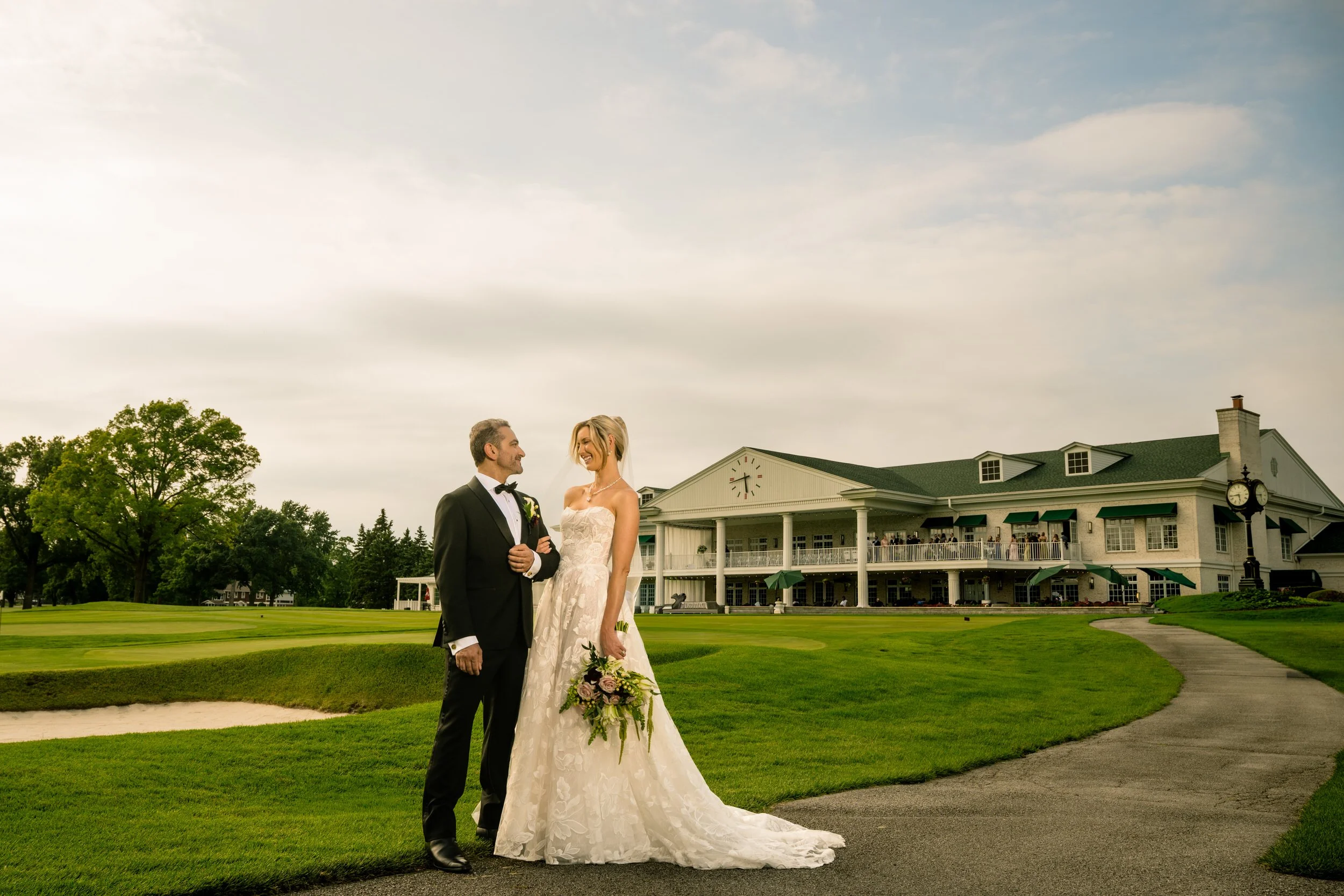 A couple looks into each other's eyes with Midlothian Country Club wedding venue in the background and all of their guests gathered on the balcony.