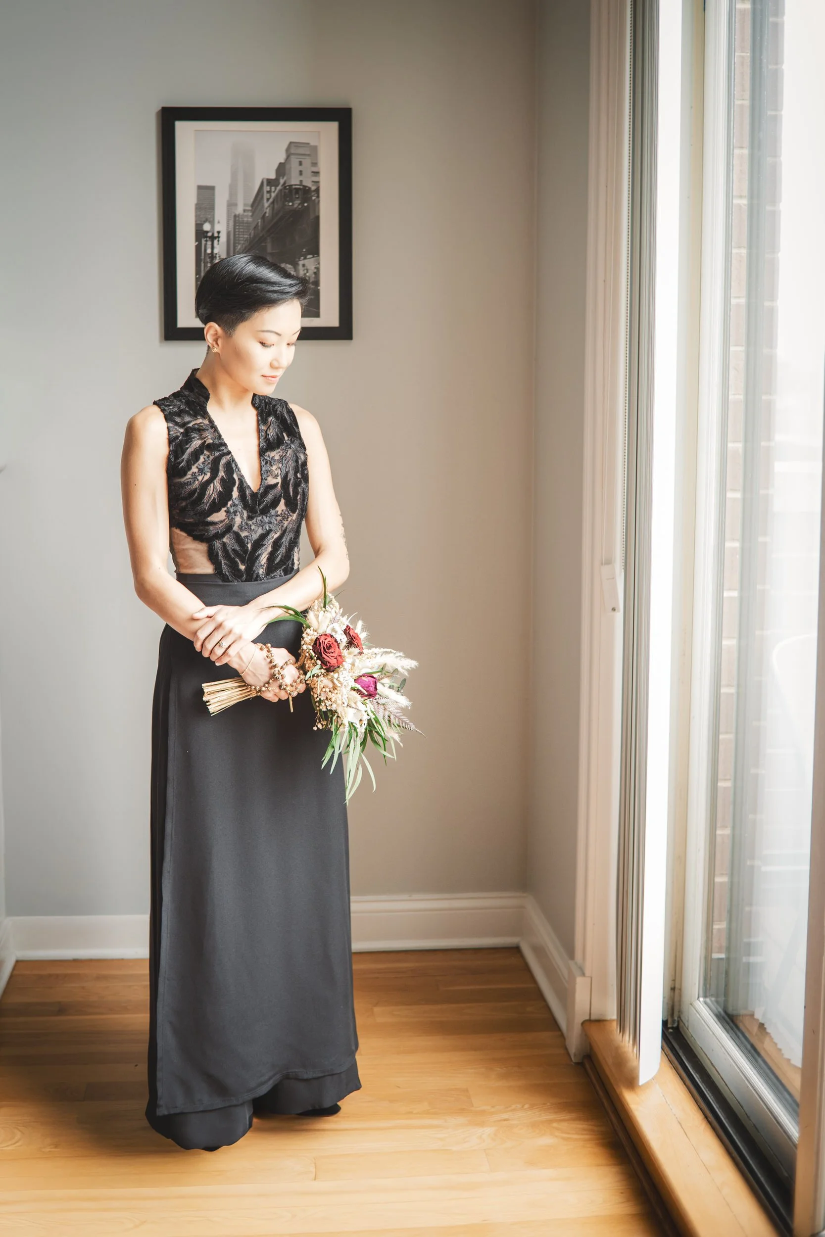 A bride in a black wedding dress clutches a bouquet of flowers while looking down in a moment of reflection.