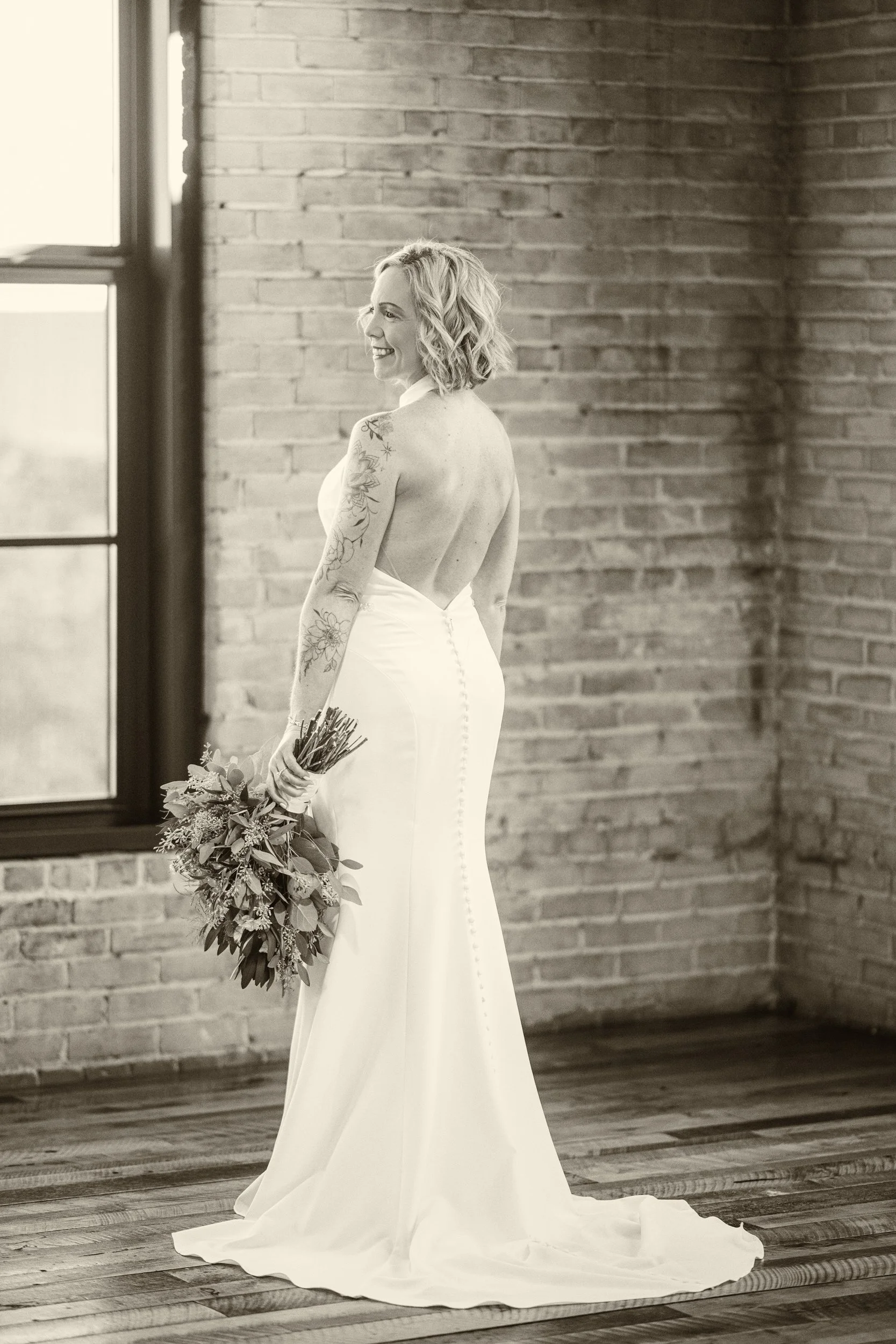A black and white image of a bride showing off the back of her dress at Journeyman Distillery in Three Oaks, Michigan.