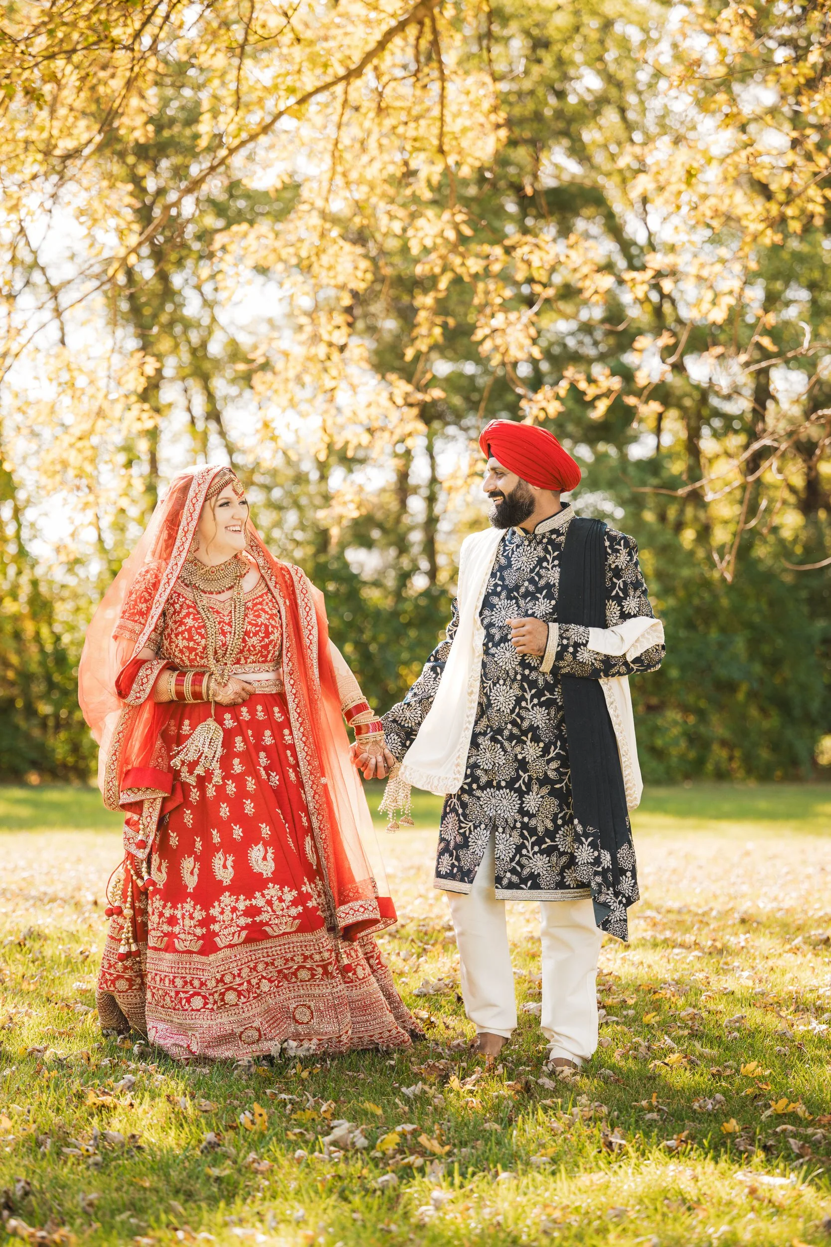 An Indian bride and groom walk in leaves in colorful wedding outfits.