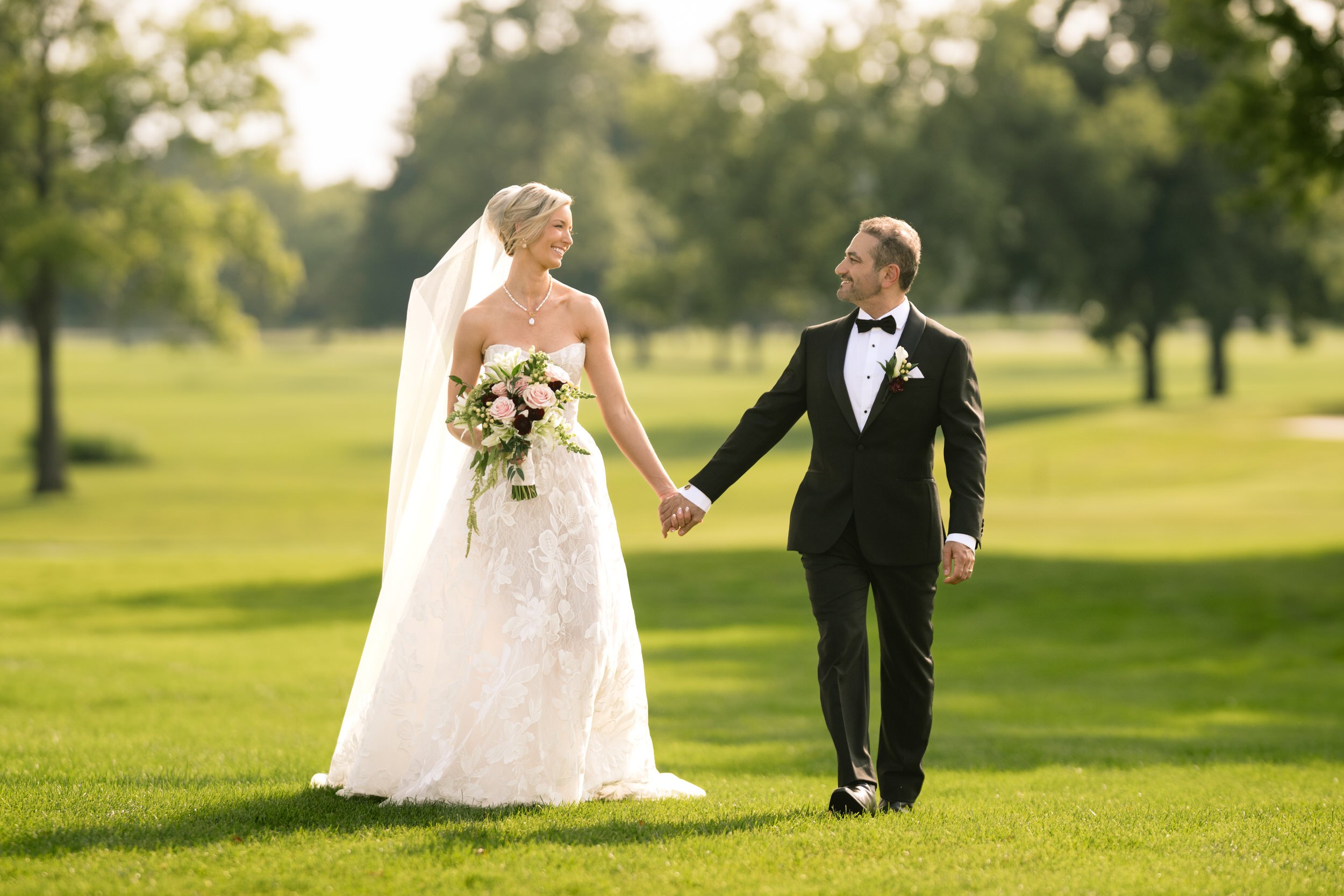 A bride and groom walk along the green grass pathway at Midlothian Country Club.