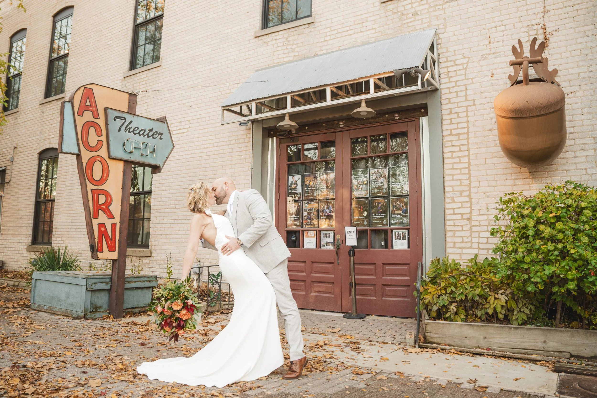 A couple in wedding attire shares a kiss in front of the Acorn Theater, a brick gem captured by a Northwest Indiana and Chicago wedding photographer, complete with its large acorn decoration and vintage sign.