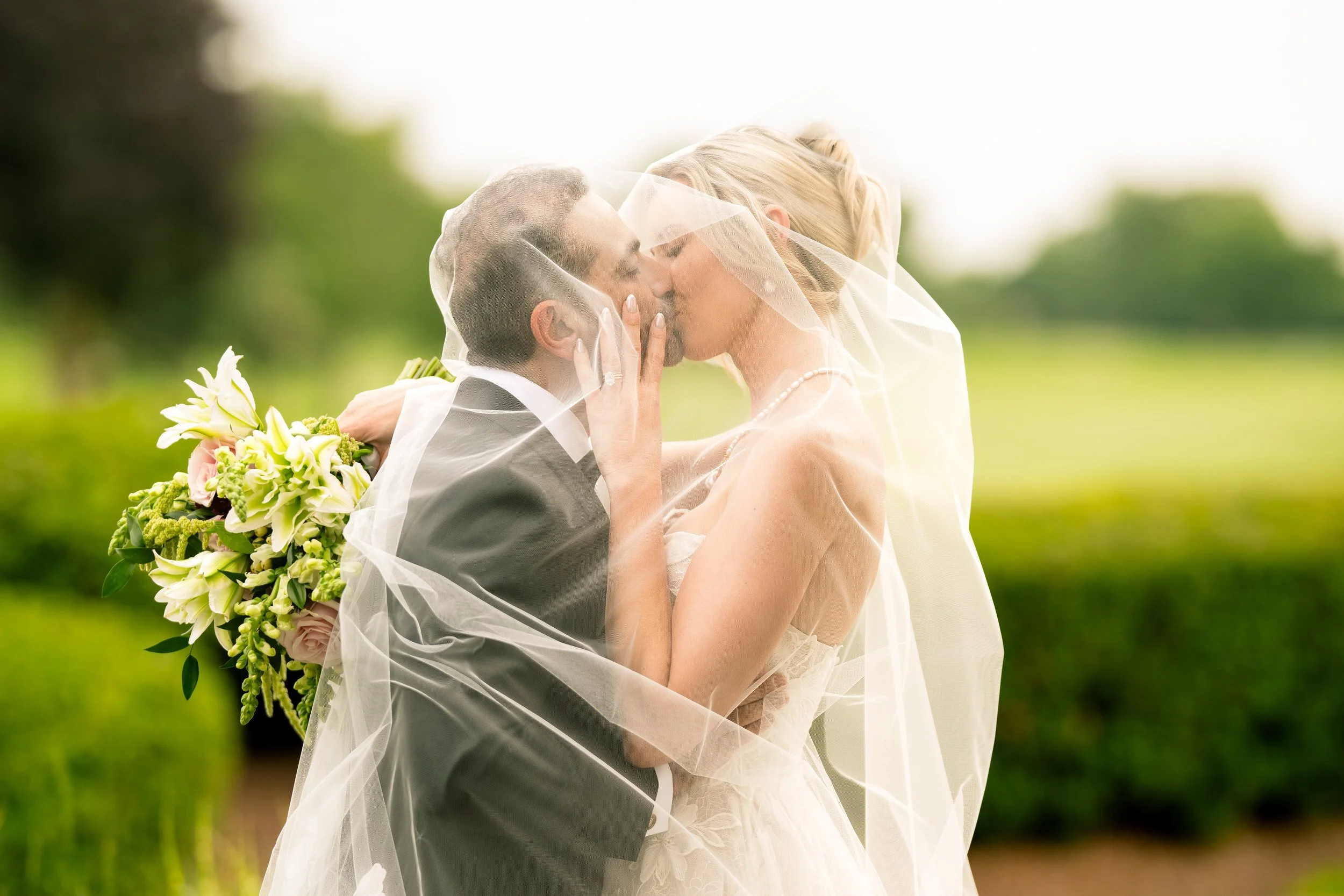 Bride and groom kiss underneath a see through veil on their wedding day.