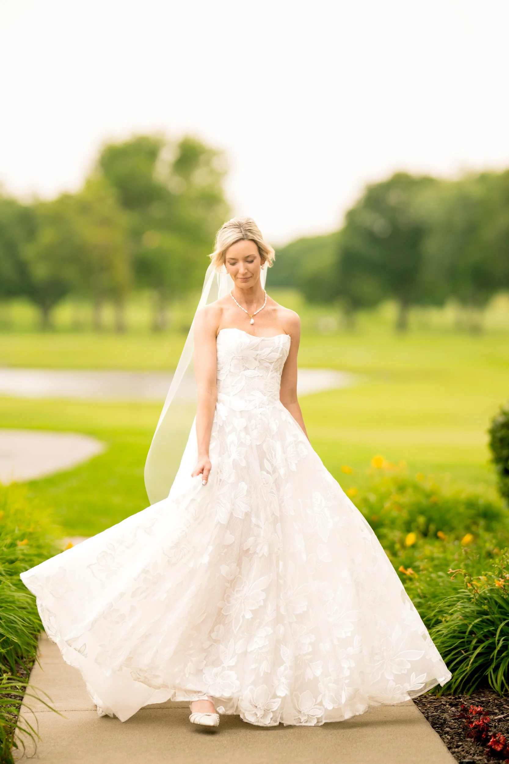 A bride tosses her dress as she walks along a path at Midlothian Country Club.