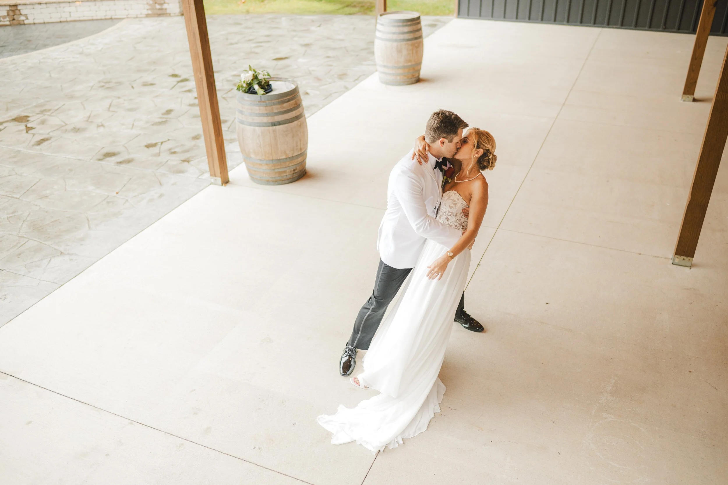 The groom dips his bride with a rustic barrel in the background.