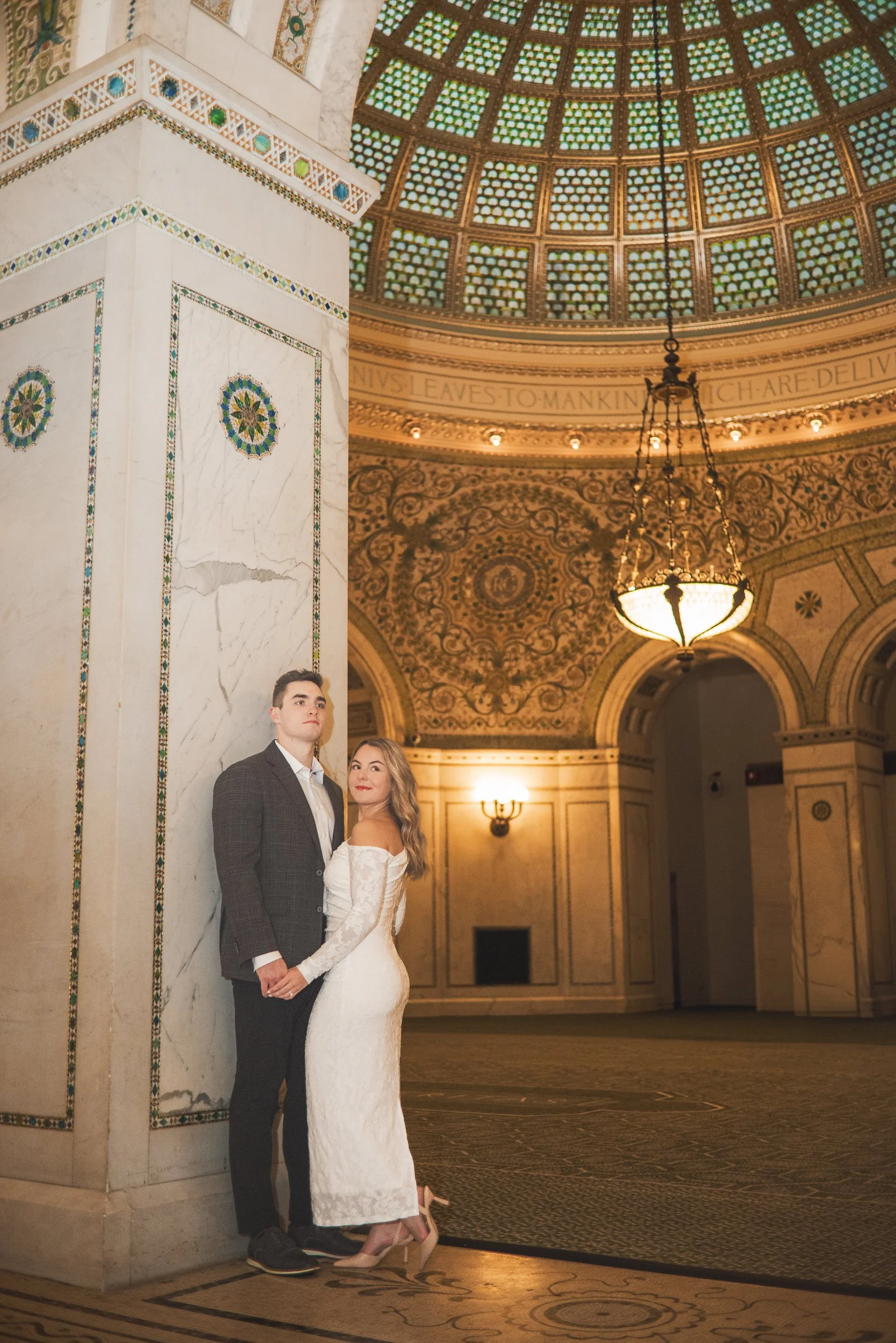 A couple stands together curing their engagement session at Chicago Cultural Center with the south dome showing above them.