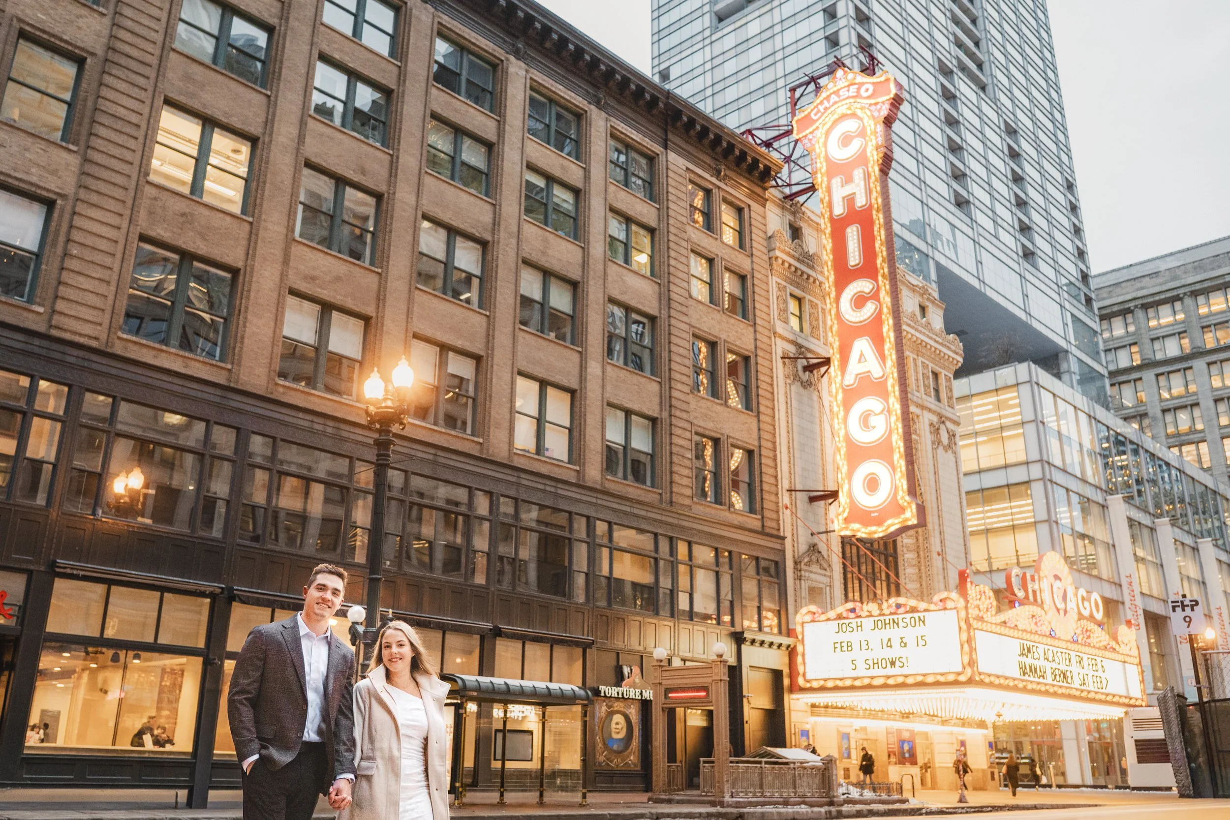 A couple crosses State Street whilde holding hands with the Chicago Theater lit up in the background.