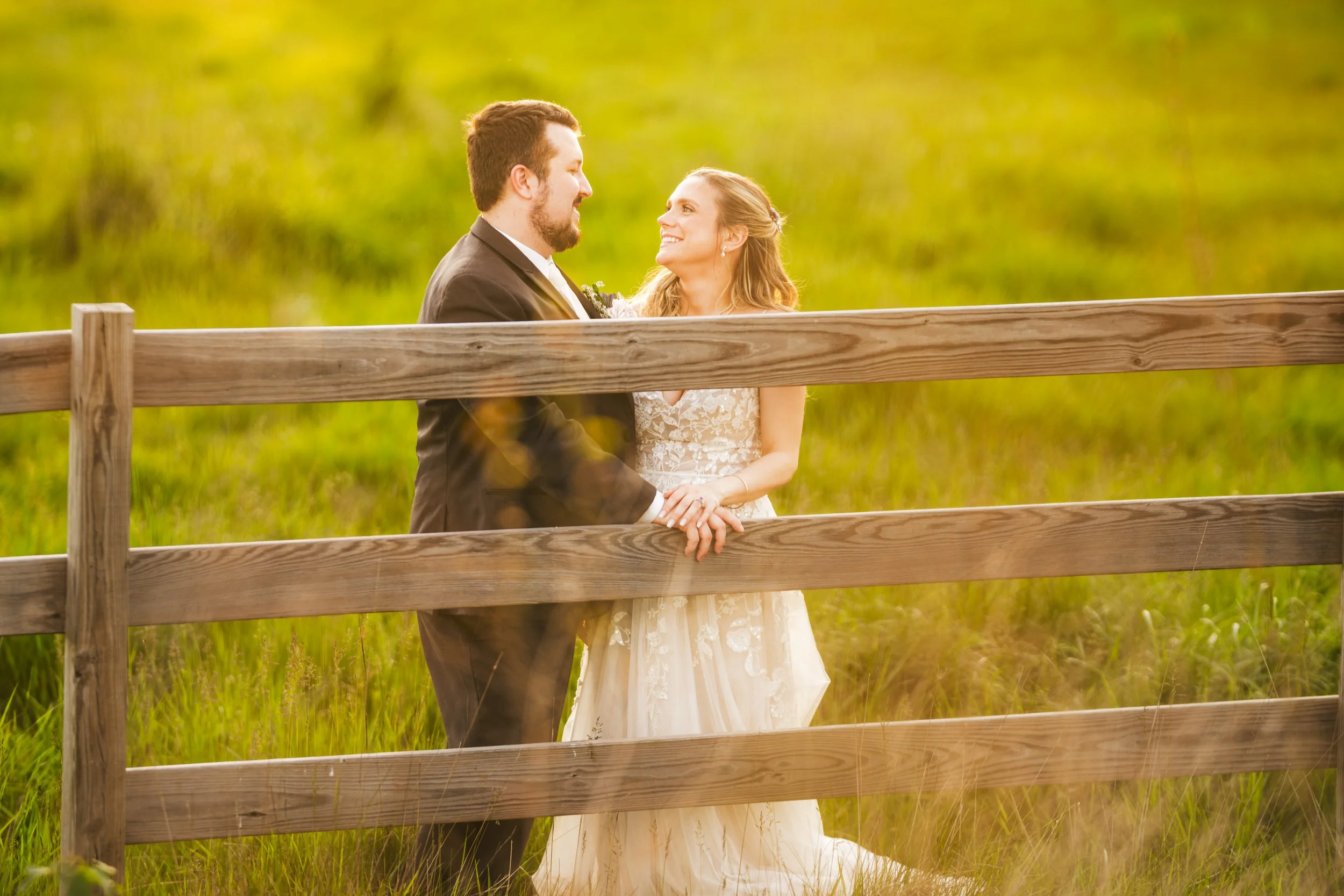 A golden hour photo of a bride and groom holding hands behind a wooden fence at The Design Barn wedding venue in Hebron, Indiana.