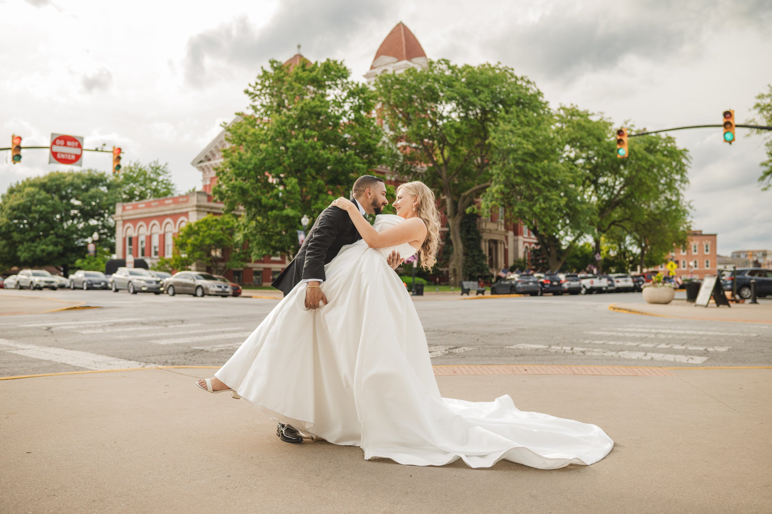 A groom dips his bride on the corner of Main Street. in Crown Point, Indiana with the old Crown Point Courthouse in the background.