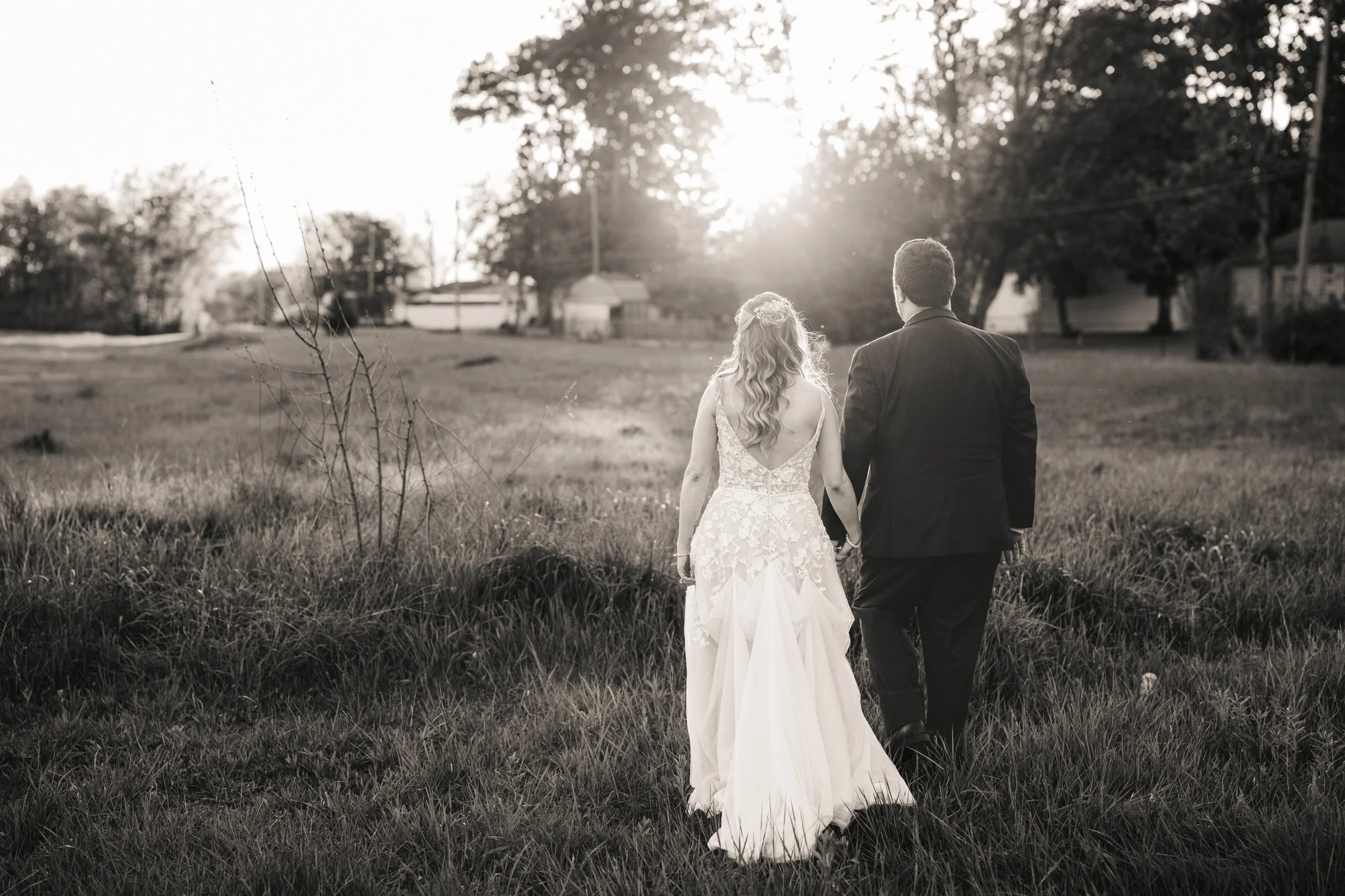A black and white, natural light wedding photo of a couple walking into the sunlight at an Indiana farm.