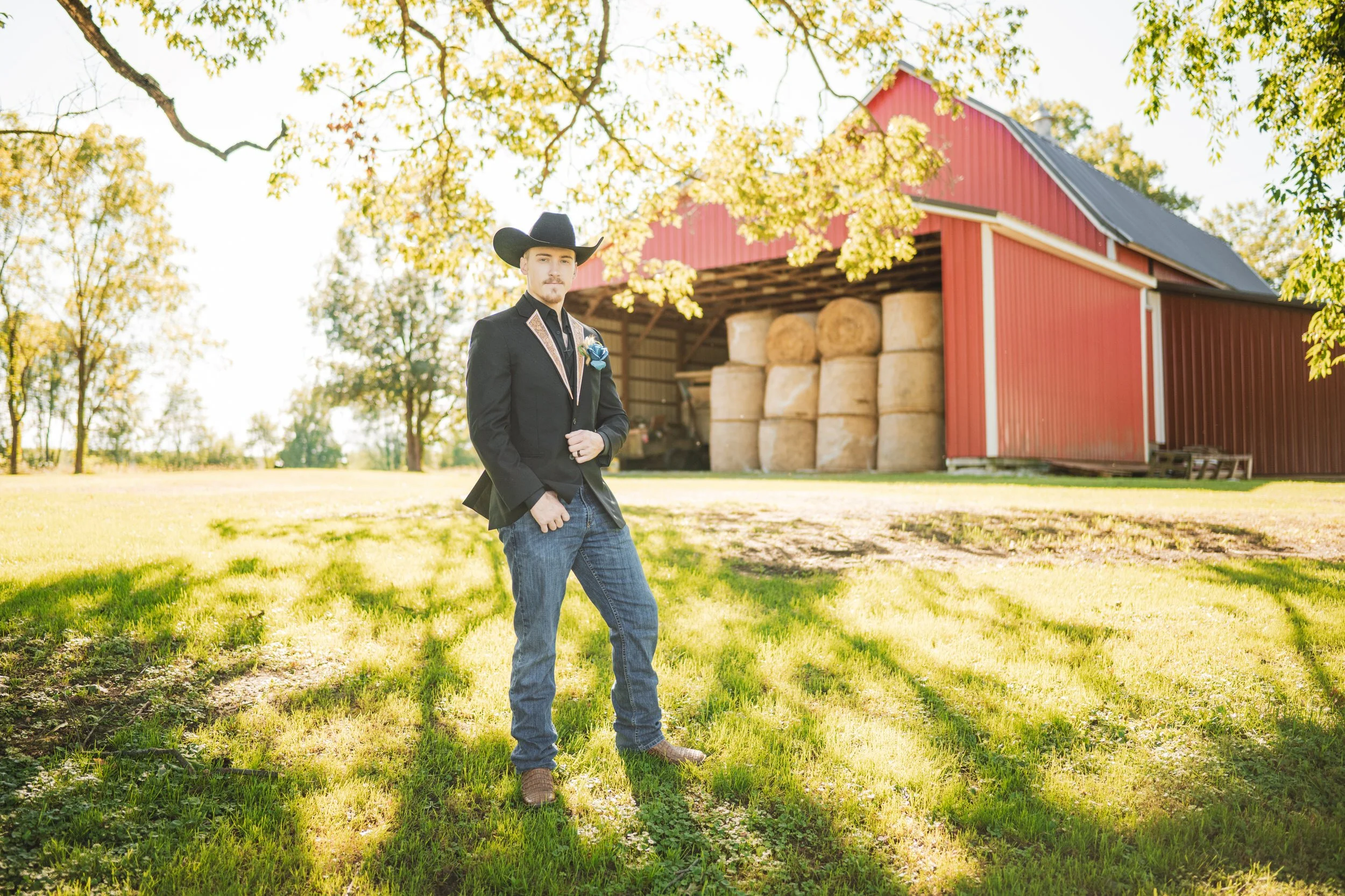 A groom in a black cowboy hat poses for the camera with farm equipment in the background.