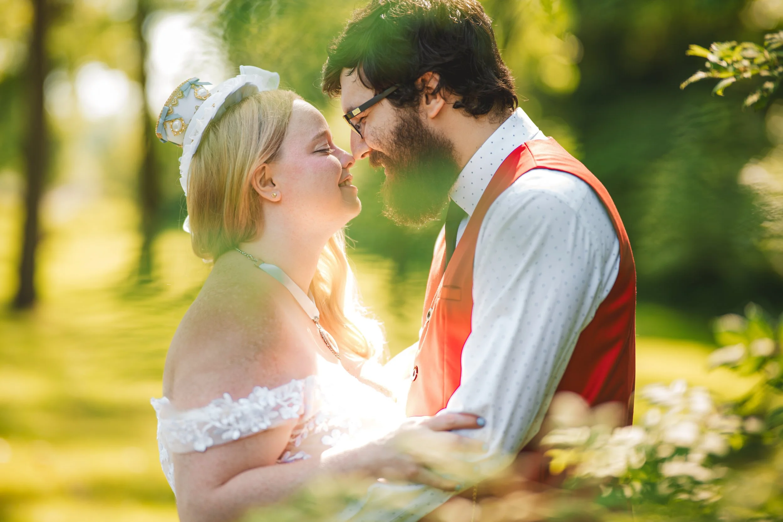 A couple dressed in wedding attire stands outdoors, holding each other closely and touching noses, surrounded by greenery and sunlight, captured by a northwest Indiana and Chicago wedding photographer.