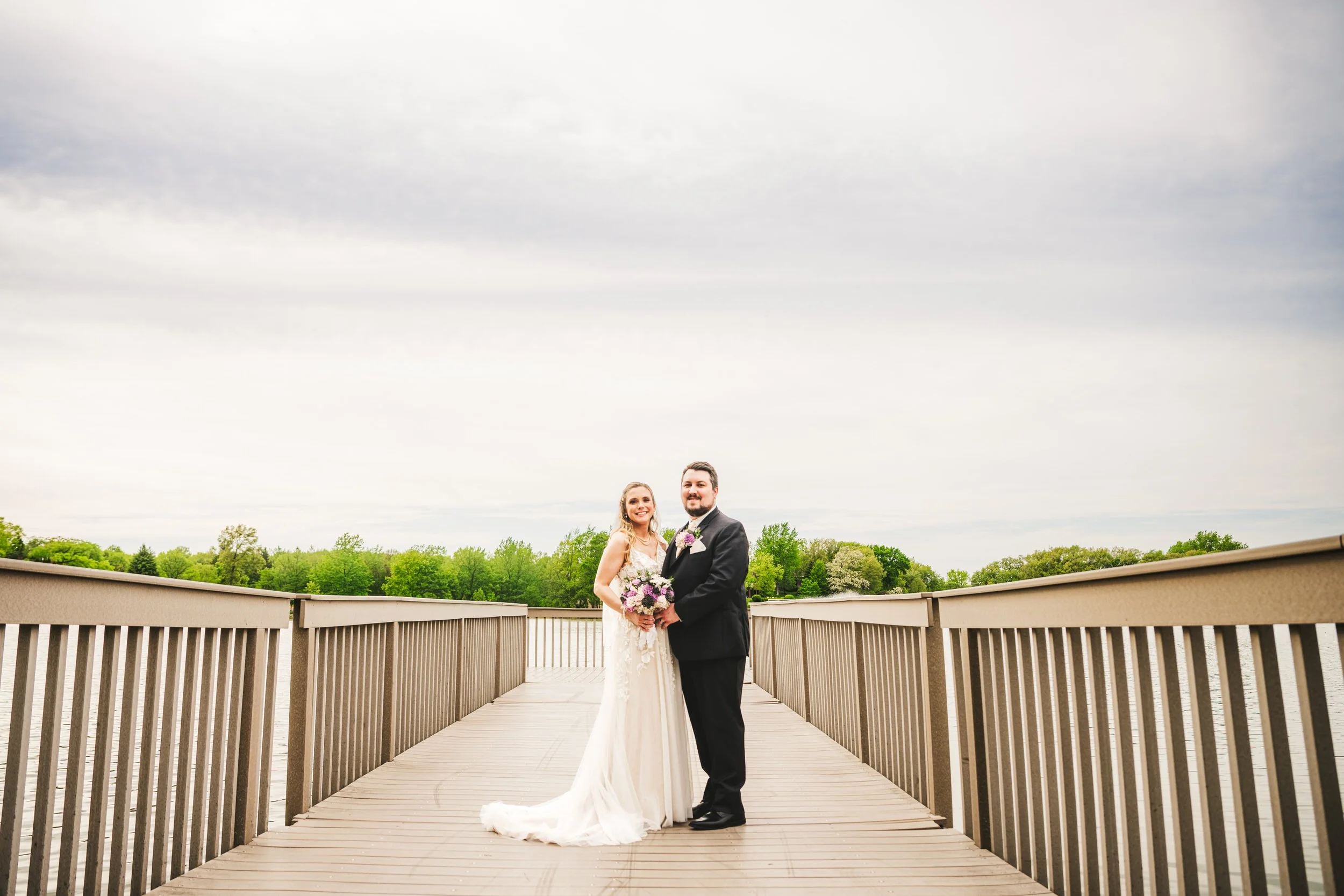 A bride and groom stand on the pier overlooking the lake at Lake Hills Park in St. John, Indiana.