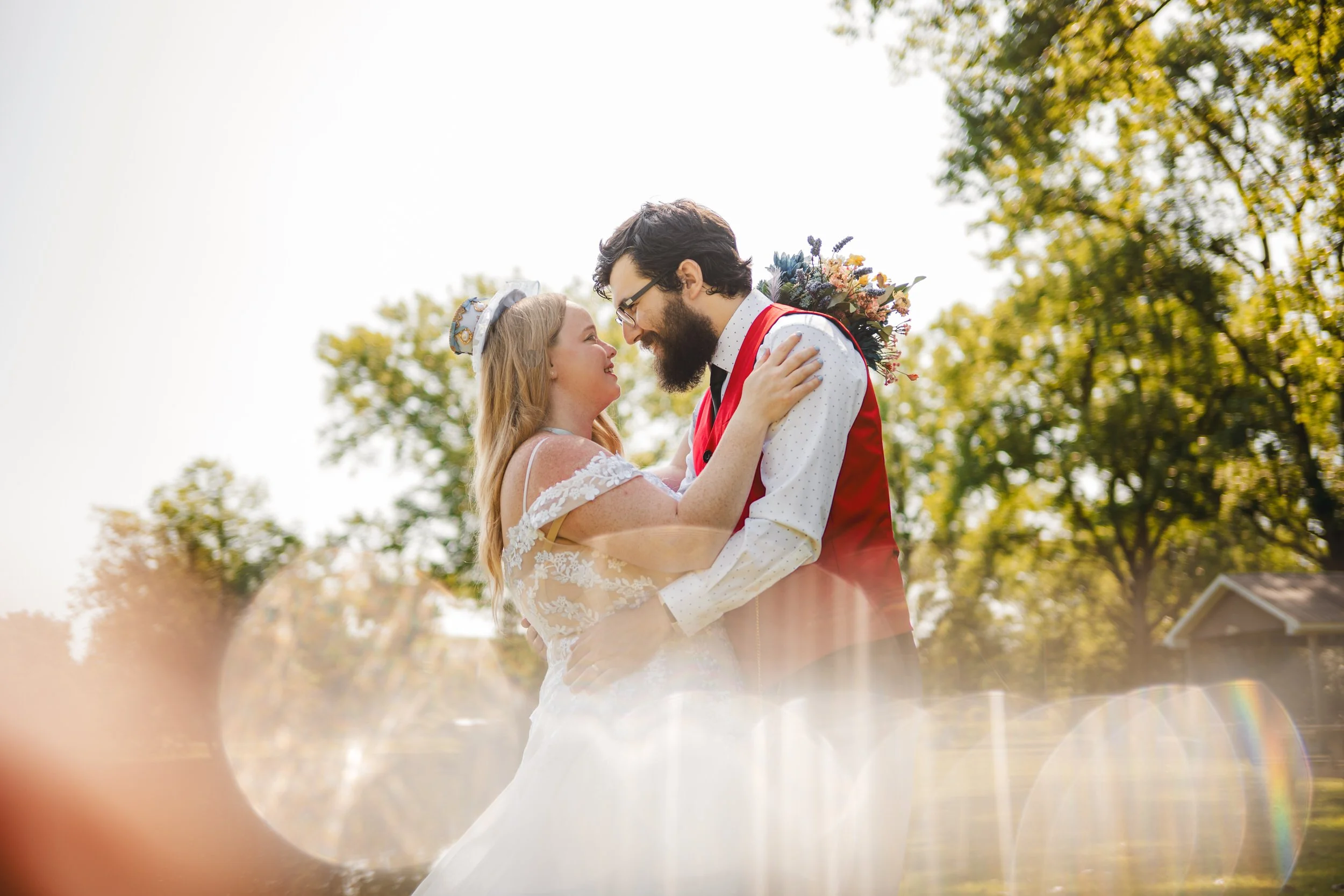 A bride and groom smile at each other and embrace outdoors, surrounded by trees and sunlight, captured by a Northwest Indiana and Chicago wedding photographer.