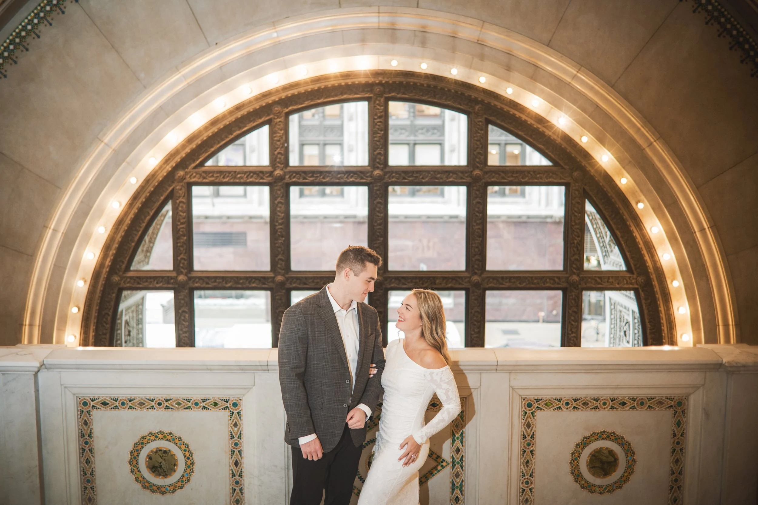 A young couple look at each other in front of the circular archway windows of the Chicago Cultural Center.