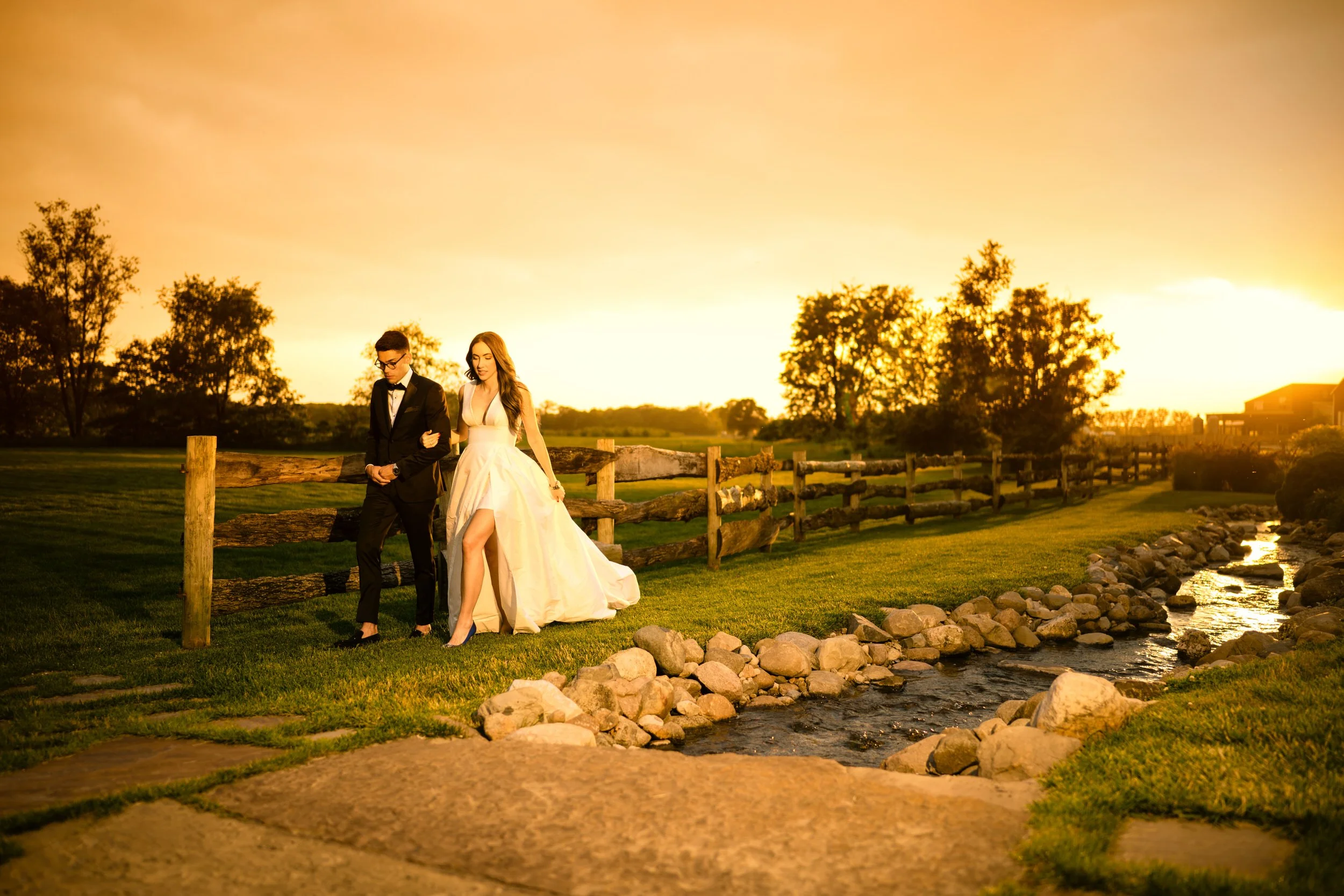 A couple walks along a fence at Fair Oaks Farms during sunset.