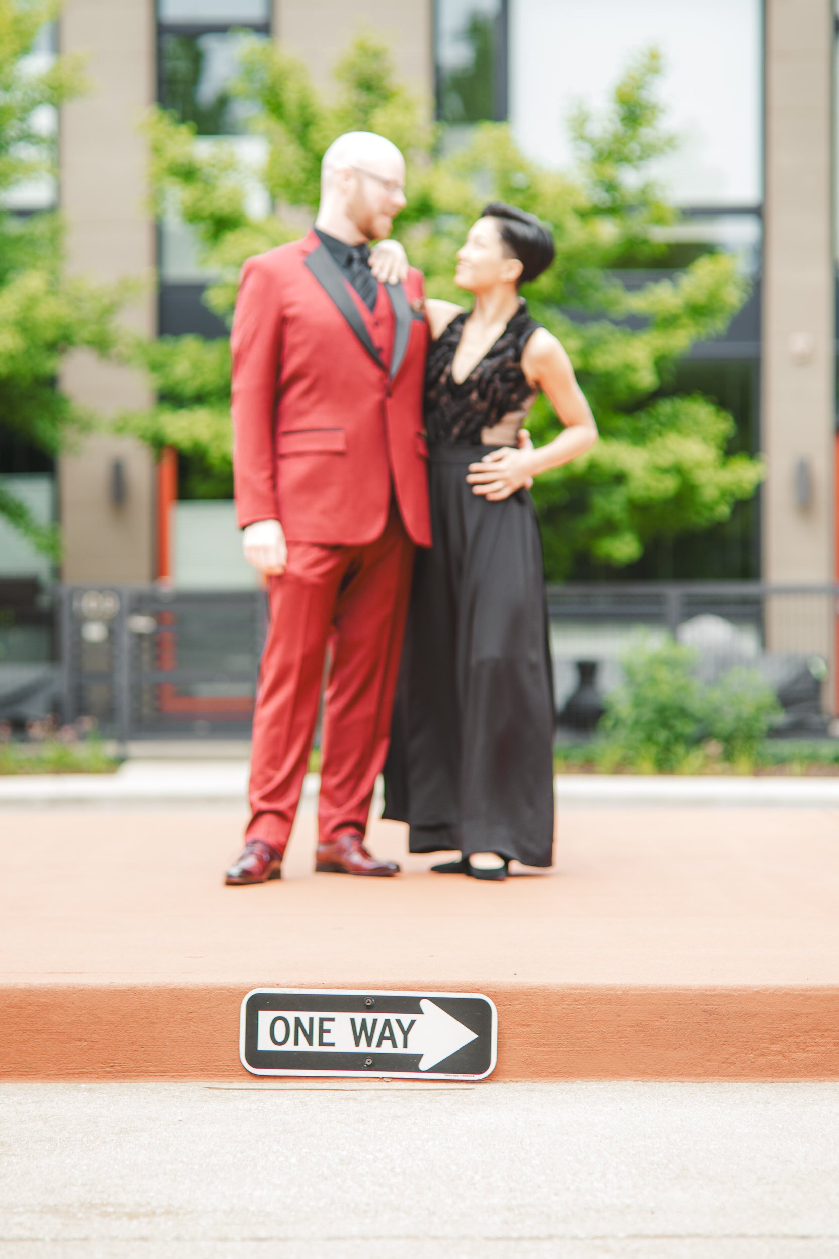 An artistic wedding portrait of a bride and groom leaning on each other with a One Way sign in focus in the foreground.