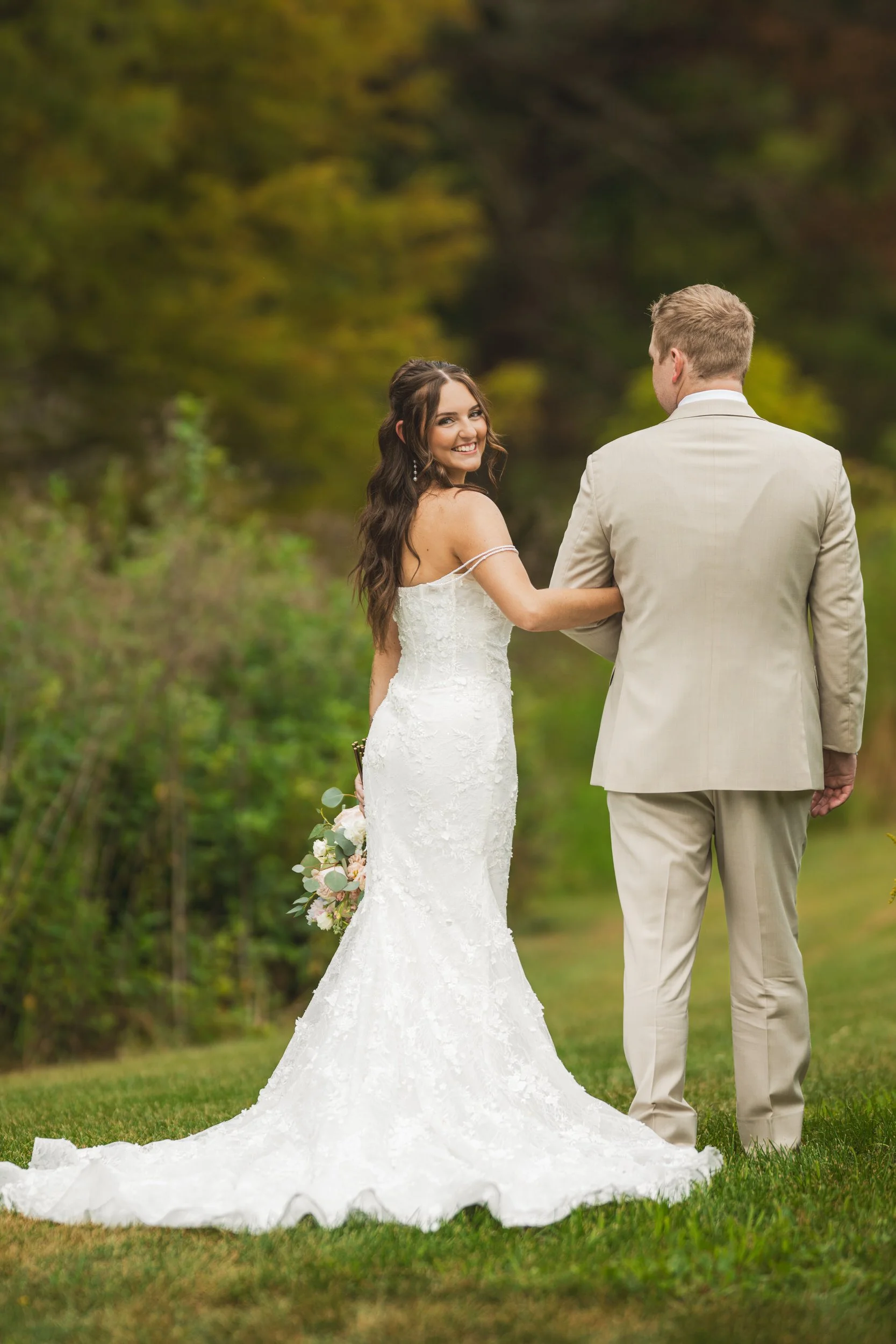 The bride looks back as she and her groom walk in nature.