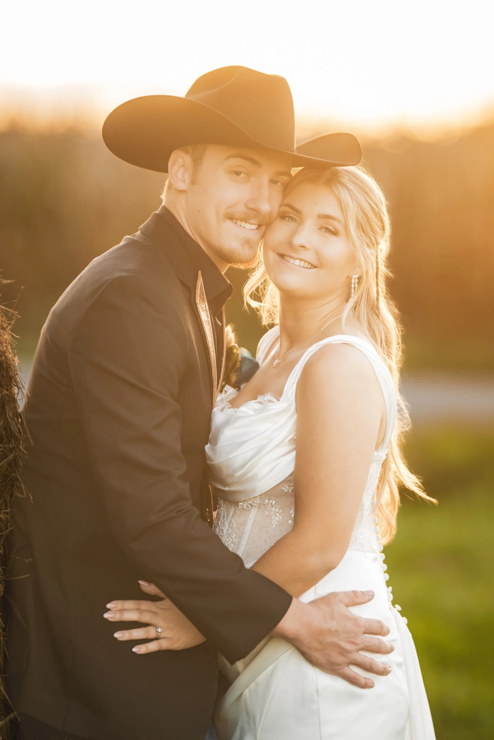 A sunset portrait of the bride and groom smiling while engulfed by golden hour light.