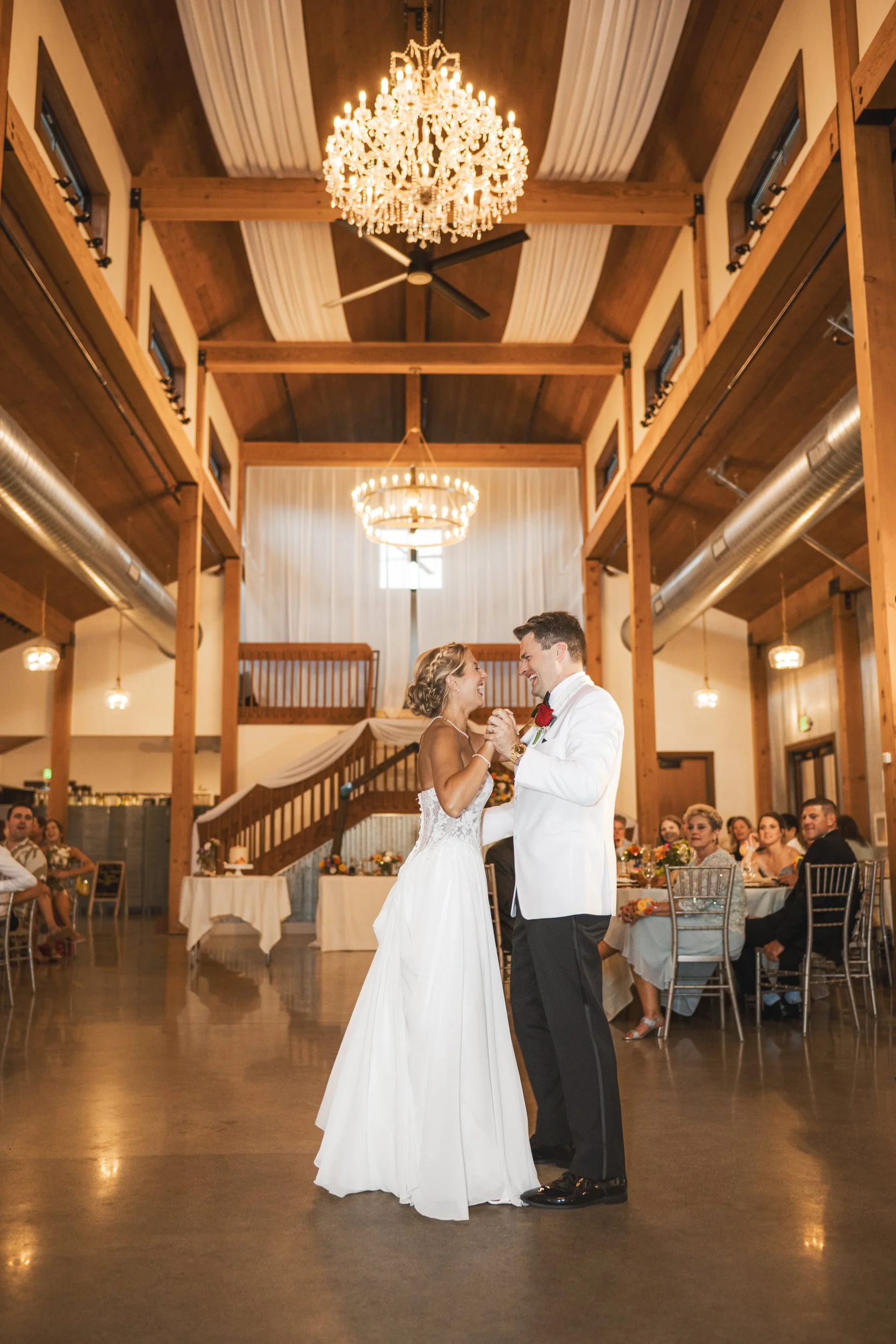 The bride and groom have their first dance in the Cedar Barn at White Oak Farm beneath the warm light of the decorative chandeliers.