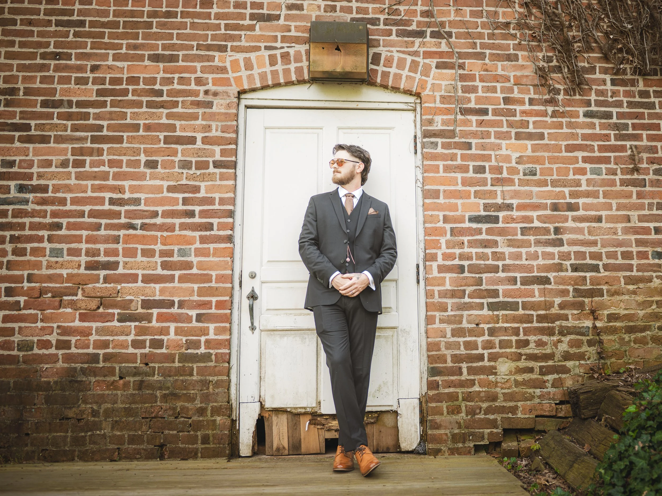 The groom leans agains the brick wall of the old grist mill at Deep River County Park.