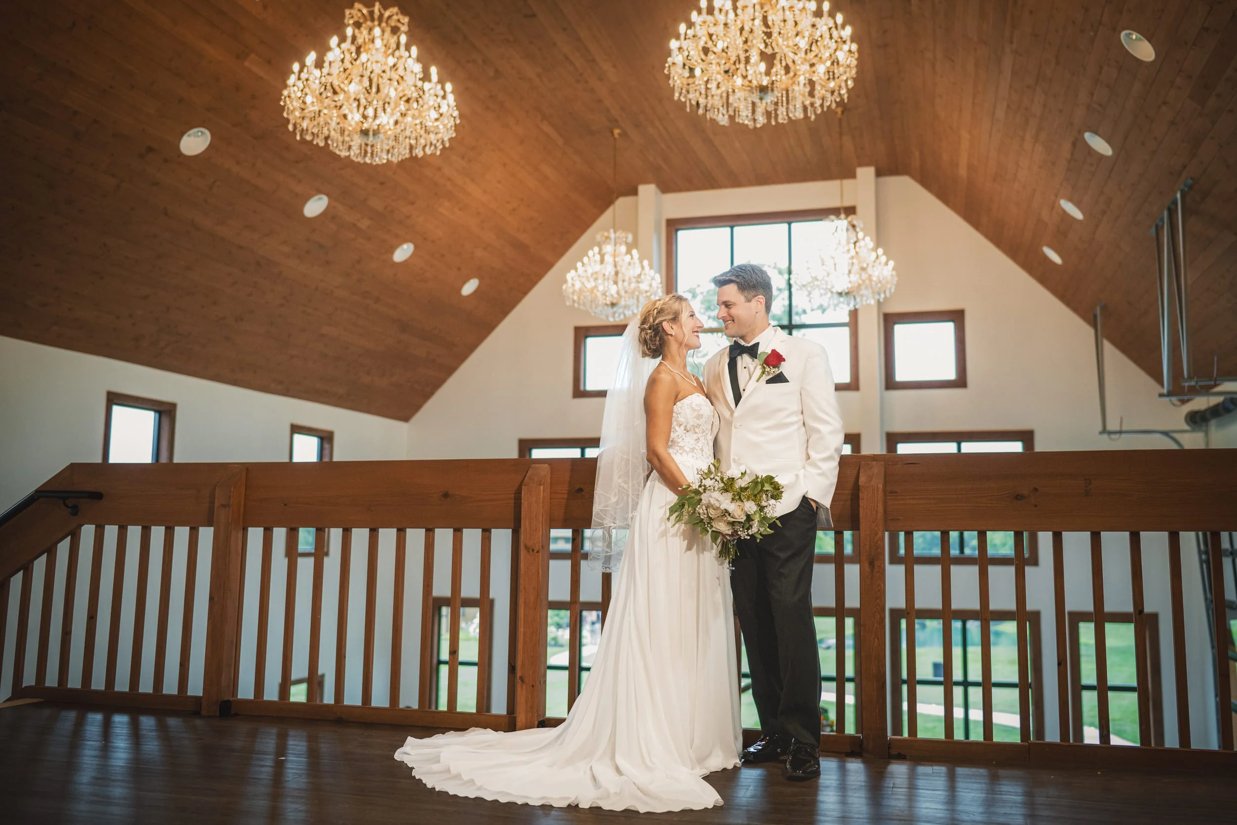 Bride and groom stand together in the loft of the Poplar Barn at White Oak Farm Venue with chandeliers above them.
