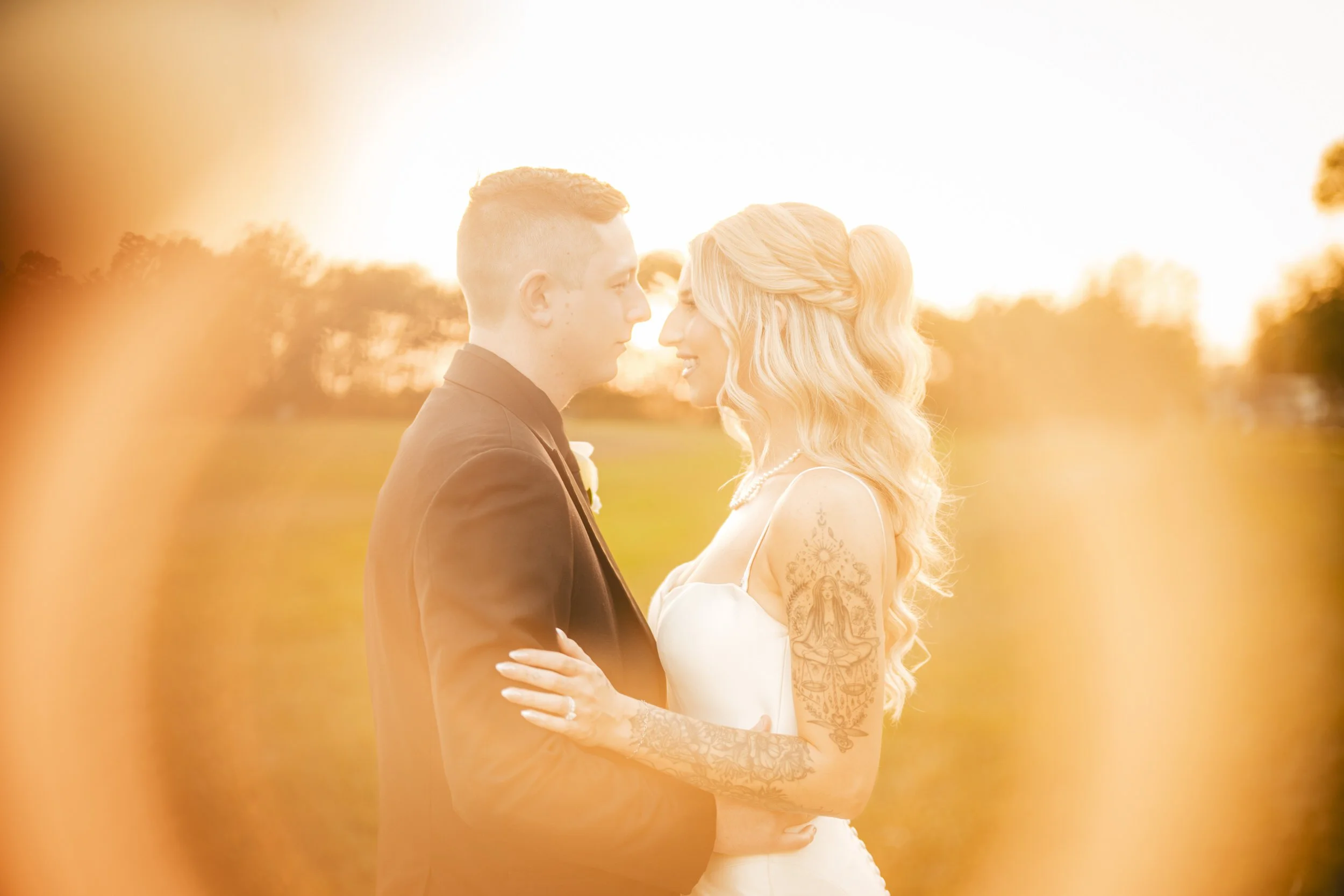 A bride and groom stand closely, facing each other in a sunlit outdoor setting, with warm golden light creating a soft, glowing effect around them—captured beautifully by a Northwest Indiana and Chicago wedding photographer.