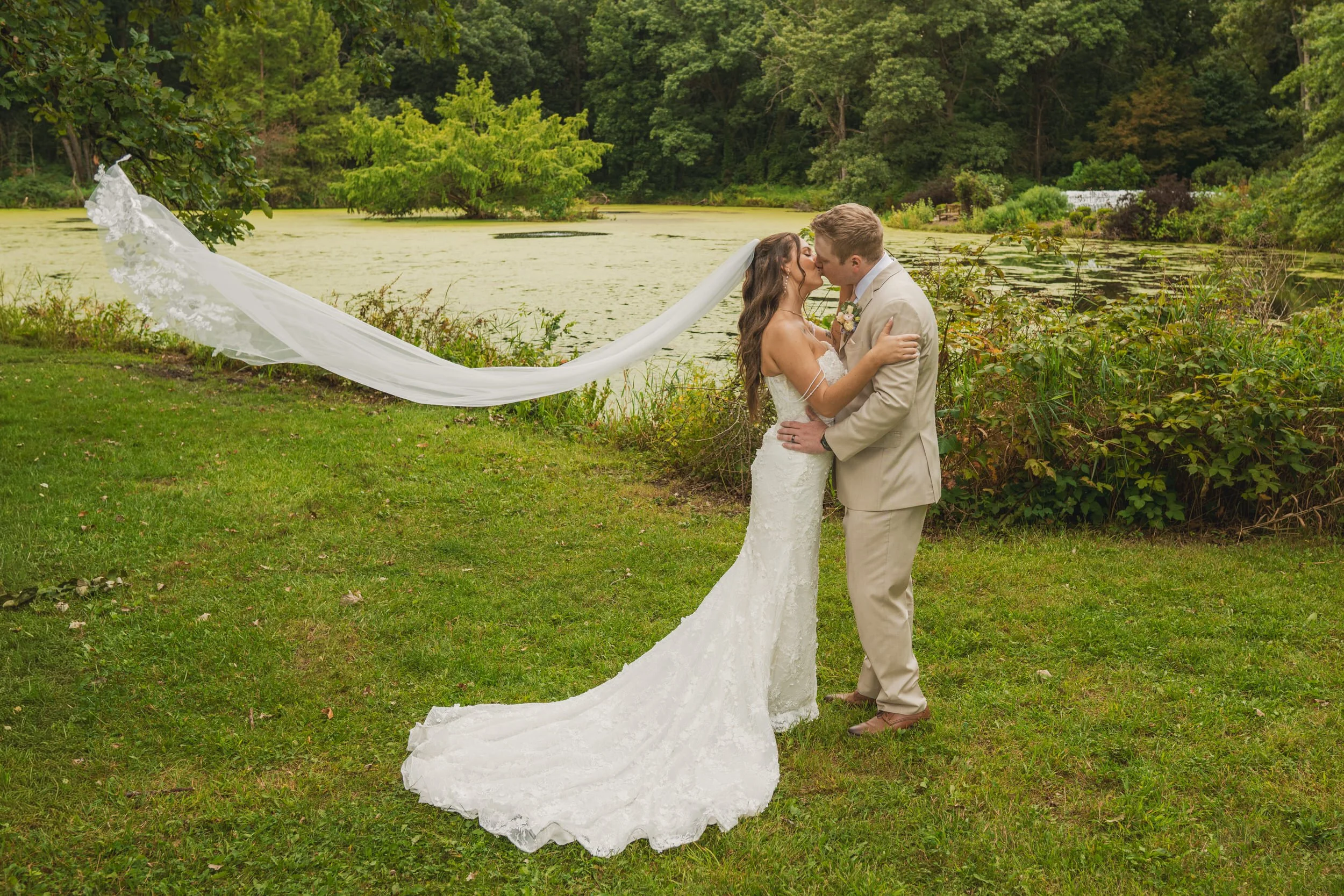 The bride's veil flies behind her as she kisses the groom surrounded by nature at Gabis Arboretum.