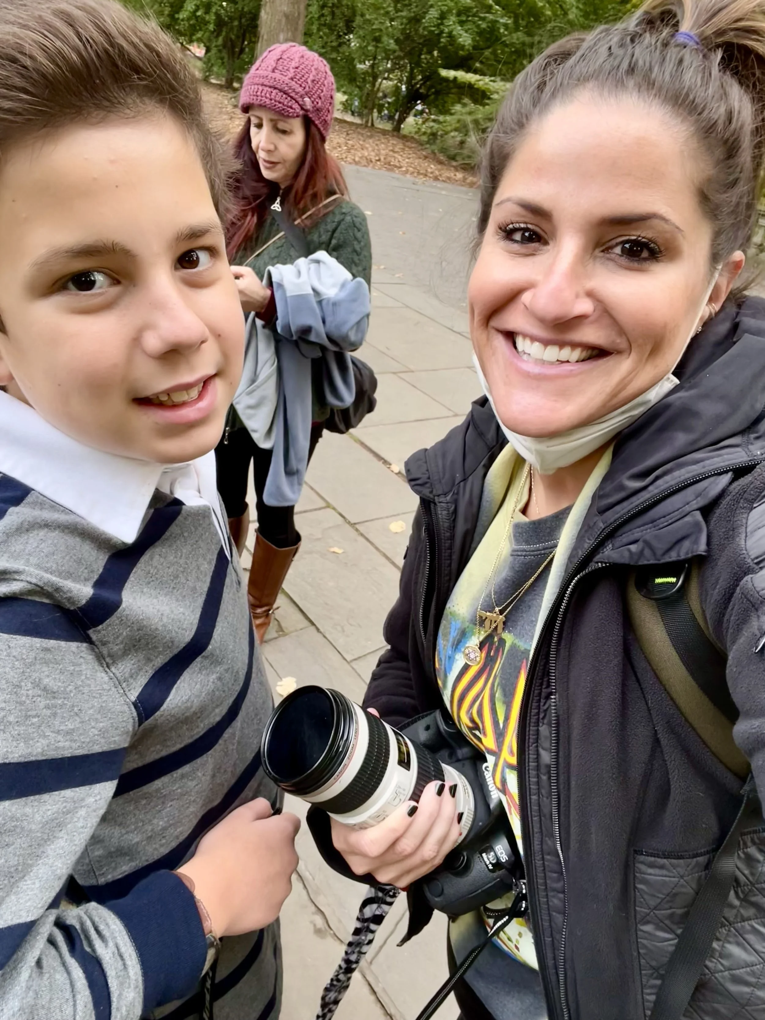 Four people outdoors, two women and two children, taking a selfie on a sidewalk surrounded by trees. Photographed by family photographer Marisa S. Cohen.