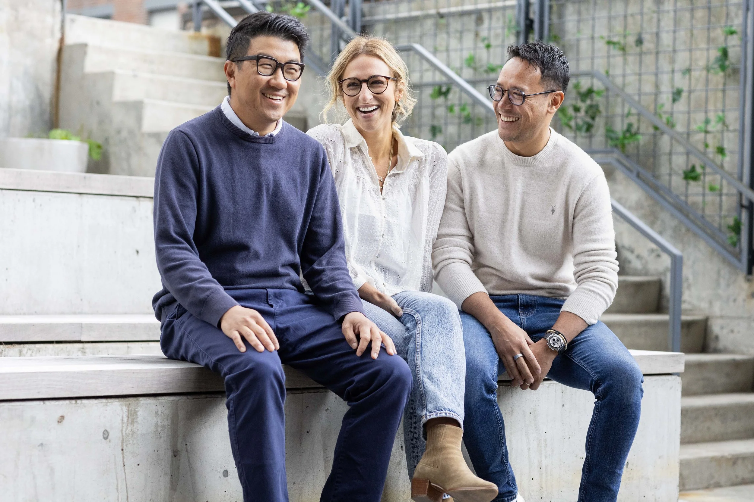 Three people sitting on concrete steps, talking and smiling with each other outdoors. Photographed by NYC family photographer Marisa S. Cohen.