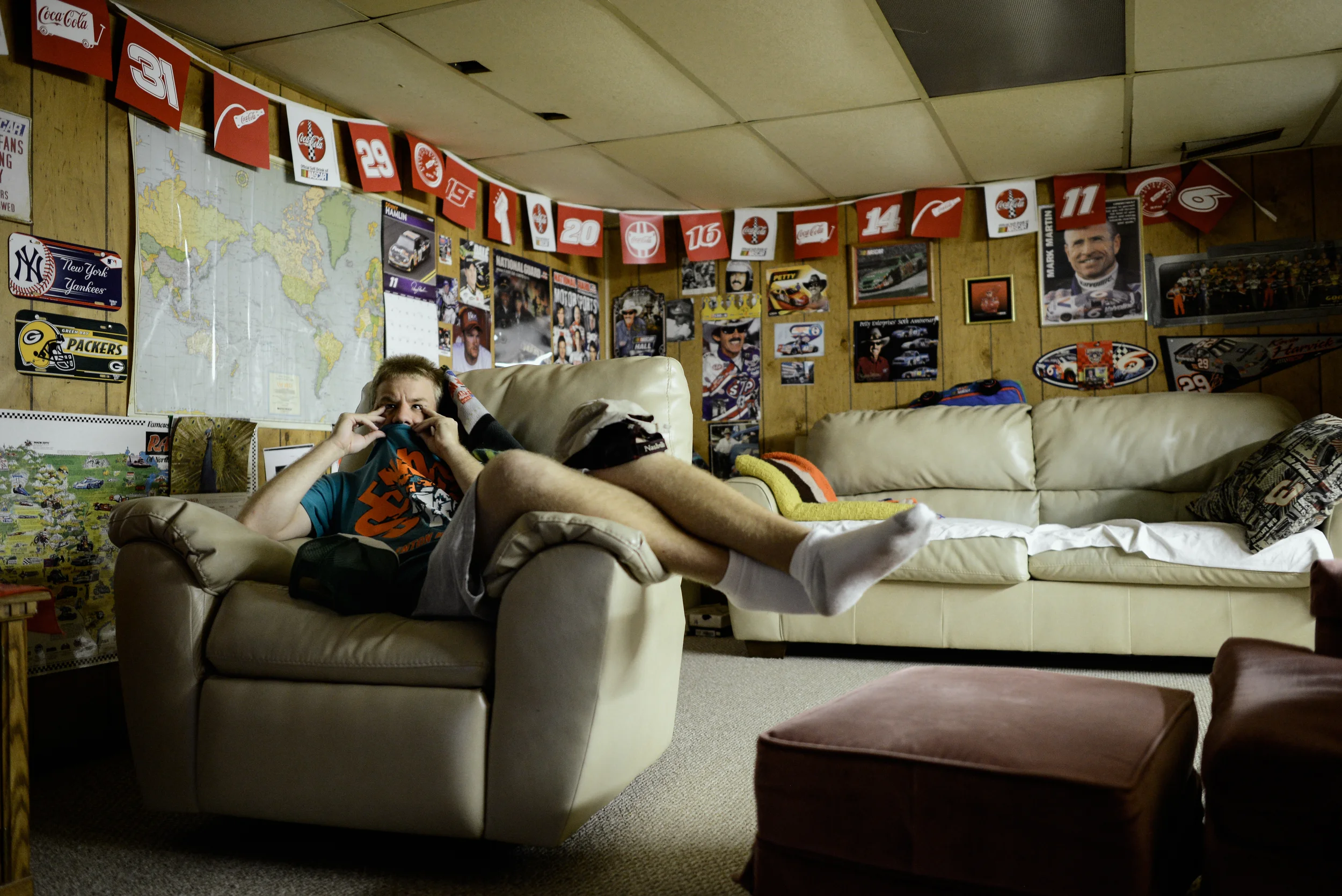 Trenton, Missouri. 2013. Dalton watches television downstairs in his safe haven decorated with his favorite sports memorabilia. He finds comfort in sitting with his hands and shirt on his face when he watches television.