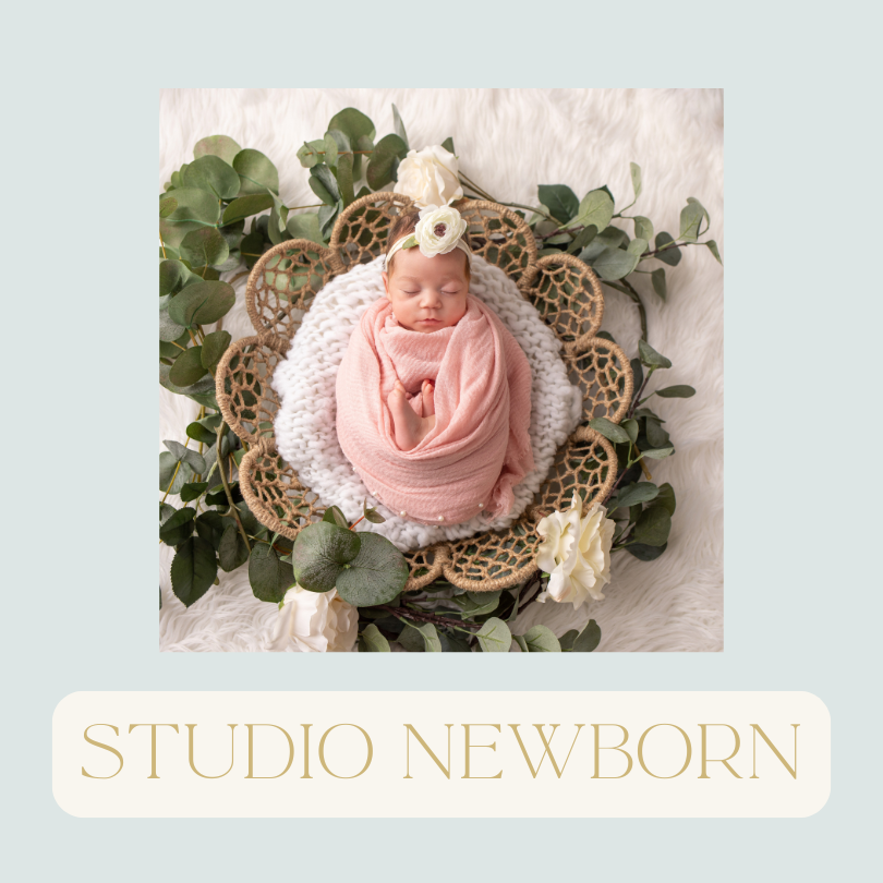 A newborn baby girl wrapped in a pink blanket, wearing a white flower headband, sleeping on a fluffy white surface surrounded by green eucalyptus leaves and white flowers, with a lace doily underneath.