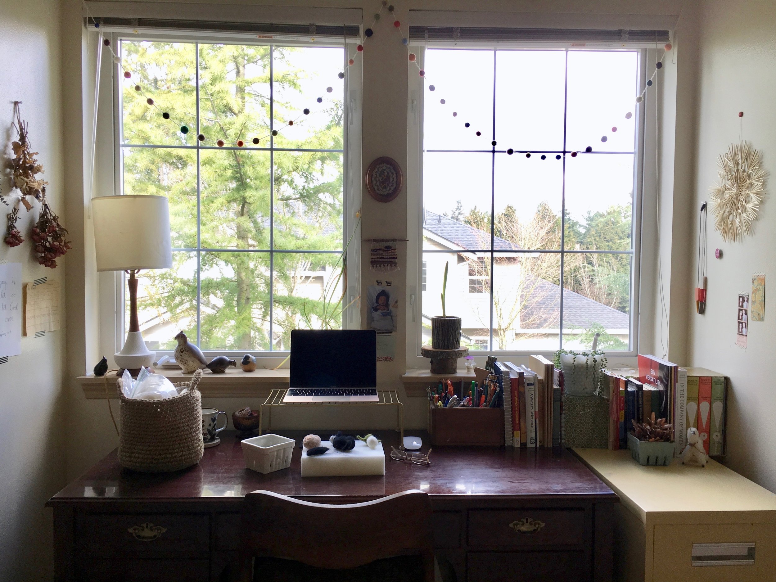 I work a lot at my desk. It serves double-duty for teaching (my other job) and running my business. I keep books as well as art supplies on top for easy access. I made the felted pom pom garland over the windows to make the space feel more fun and colorful, and the small weaving I made on our road trip moving to the Pacific Northwest from Ohio; it's inspired by North Dakota. Most other items here in this view are pieces of inspiration I have thrifted; they make me happy or inspire my work in some way.