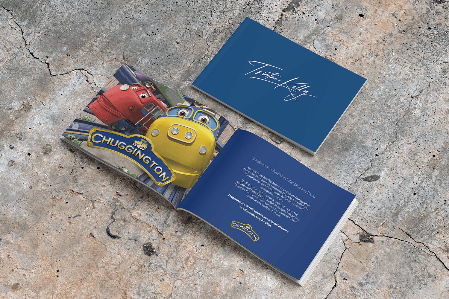 Open booklet with colorful animated cars and the Chuggington logo on the left page, and a blue cover with the name Tristan Kelly on the right page, lying on a cracked concrete surface.