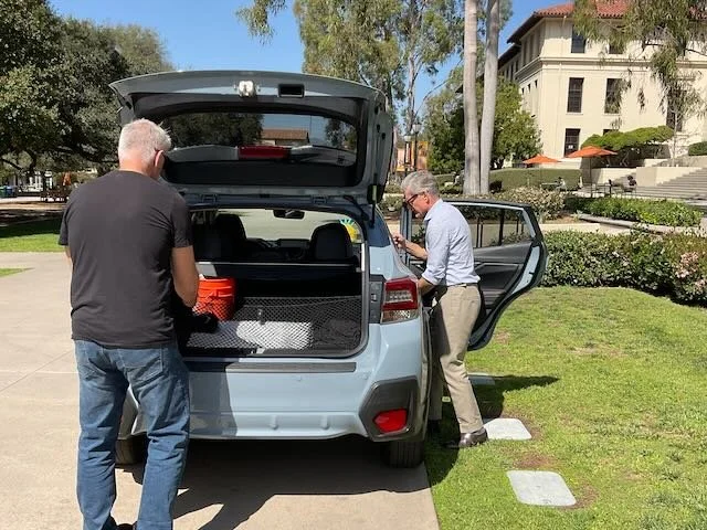  There’s DAD, removing a box from the back as his DAUGHTER takes her LAUNDRY BASKET out of the backseat. 